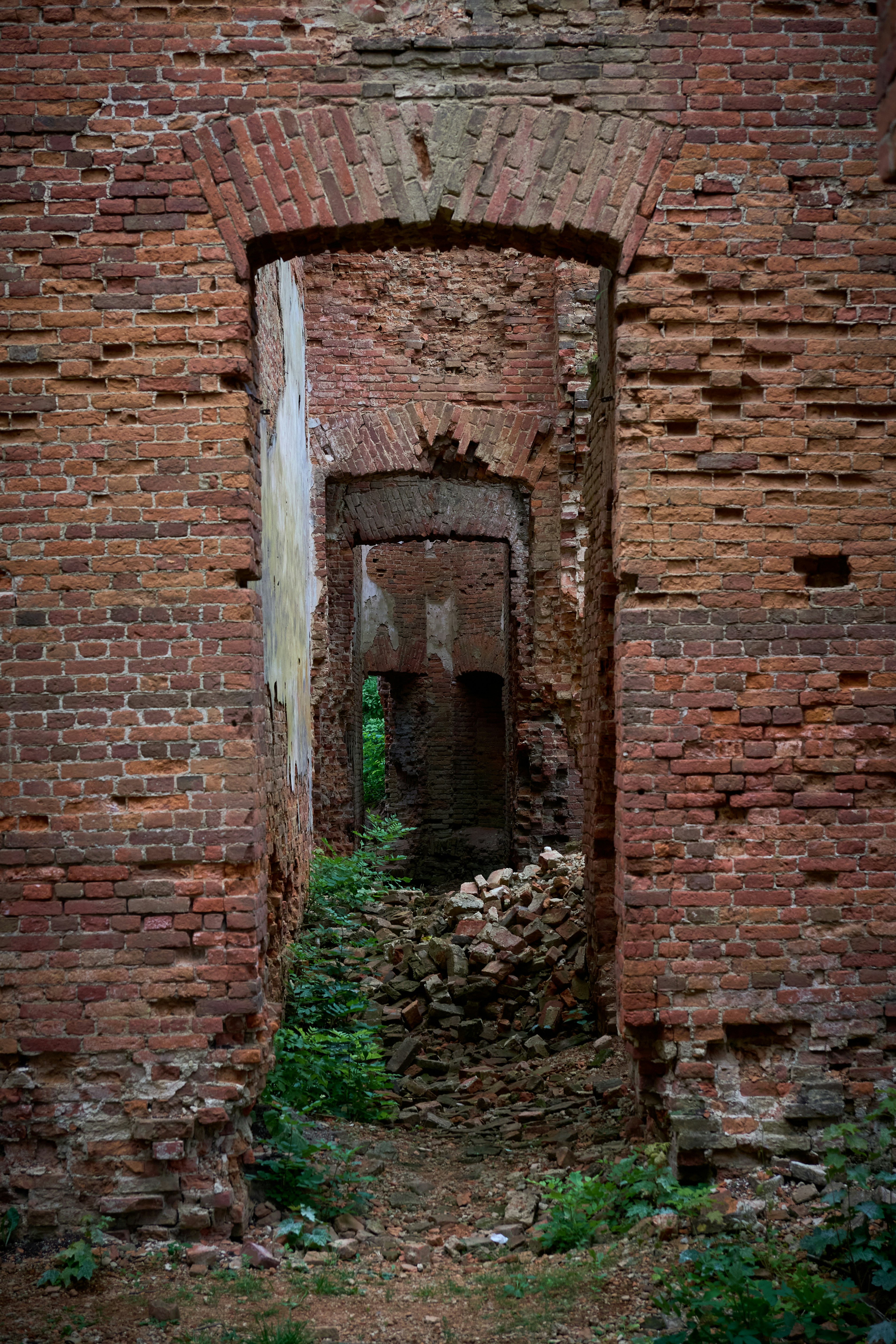 A series of arched doorways through a crumbling red brick ruin with green plants
