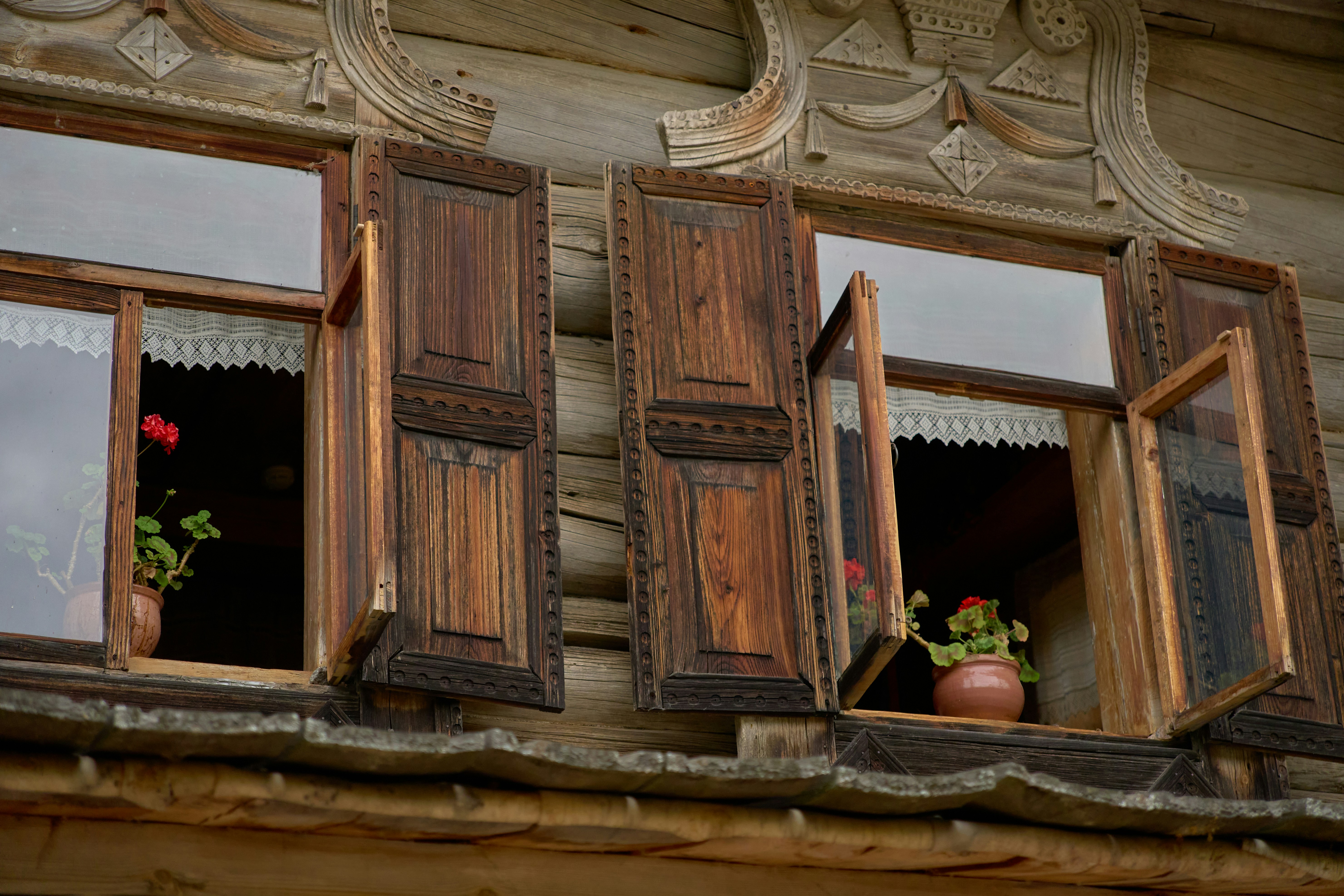 Two open wooden windows with carved shutters on a rustic log cabin wall