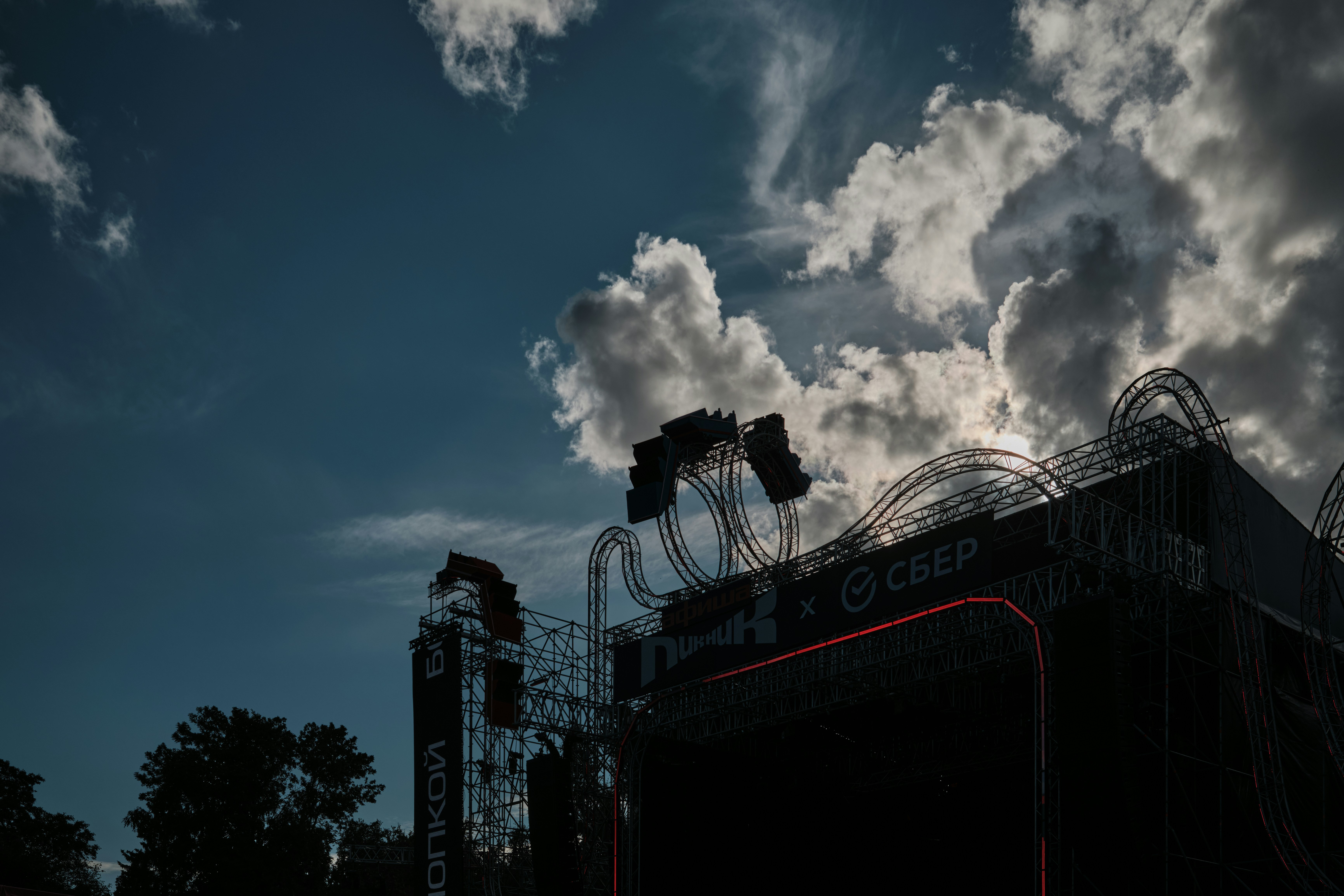 A metal concert stage structure silhouetted against a cloudy blue sky