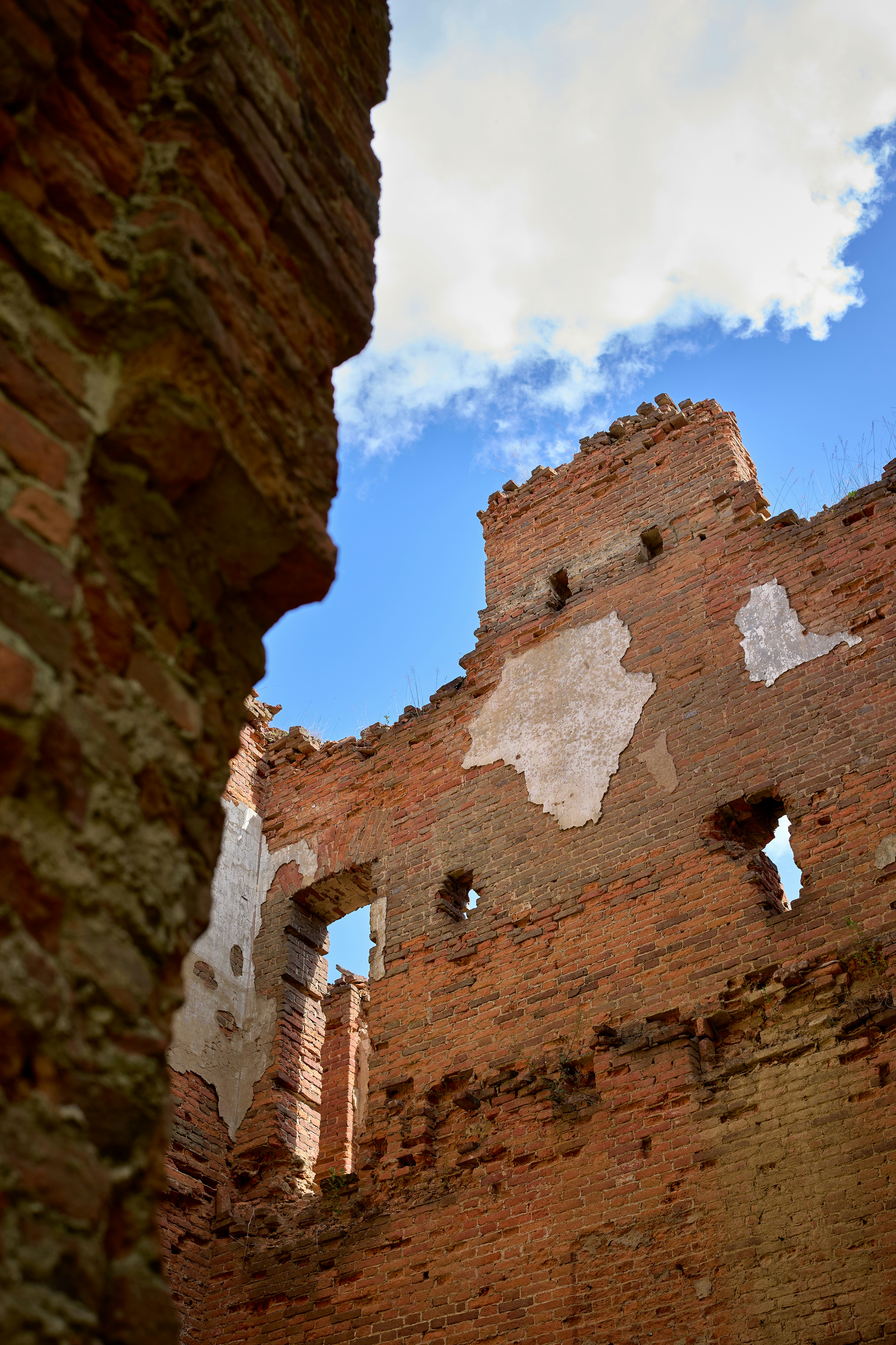 Ruined red brick walls with patches of plaster against a bright blue sky