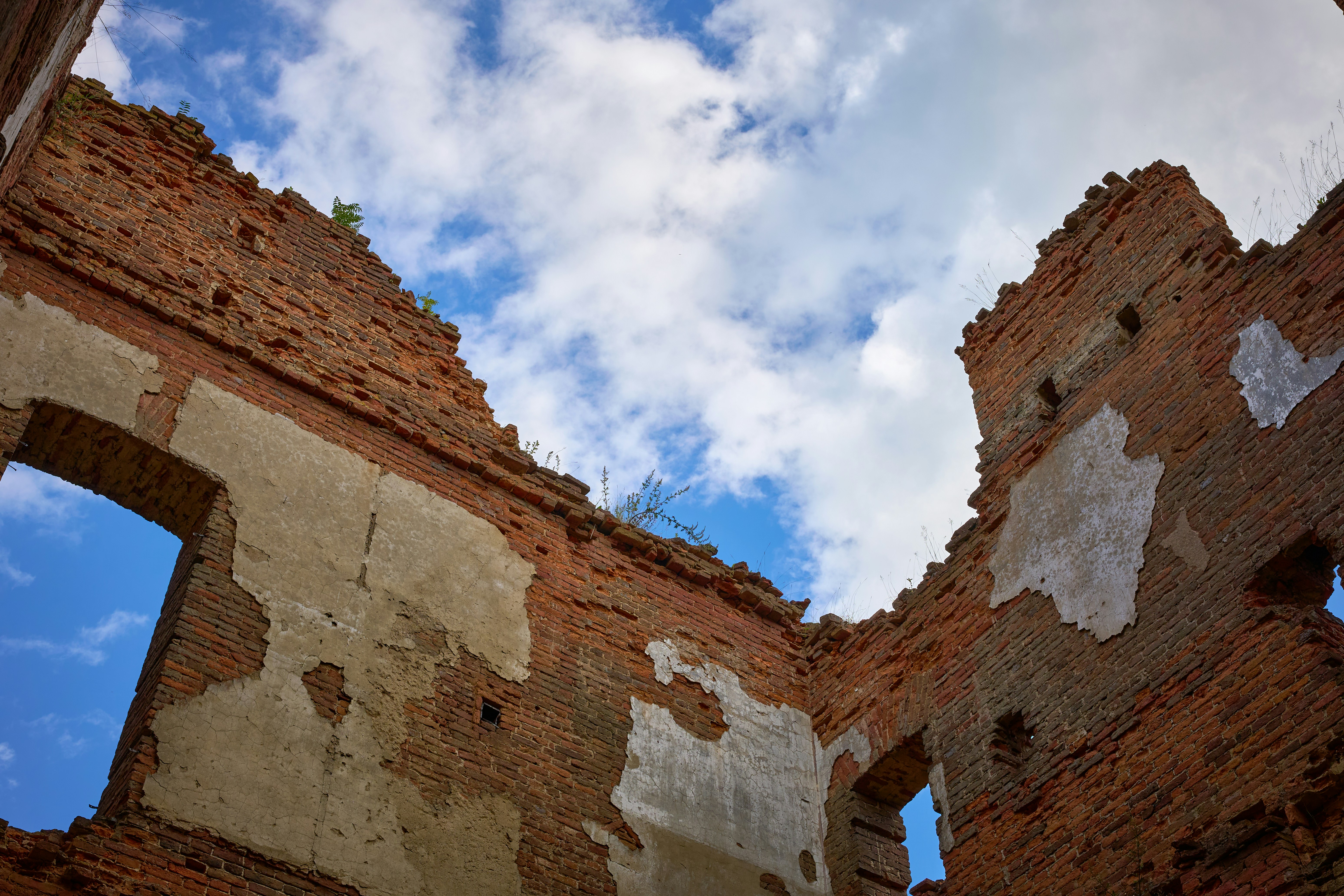 Ruined red brick walls with patches of plaster against a blue cloudy sky