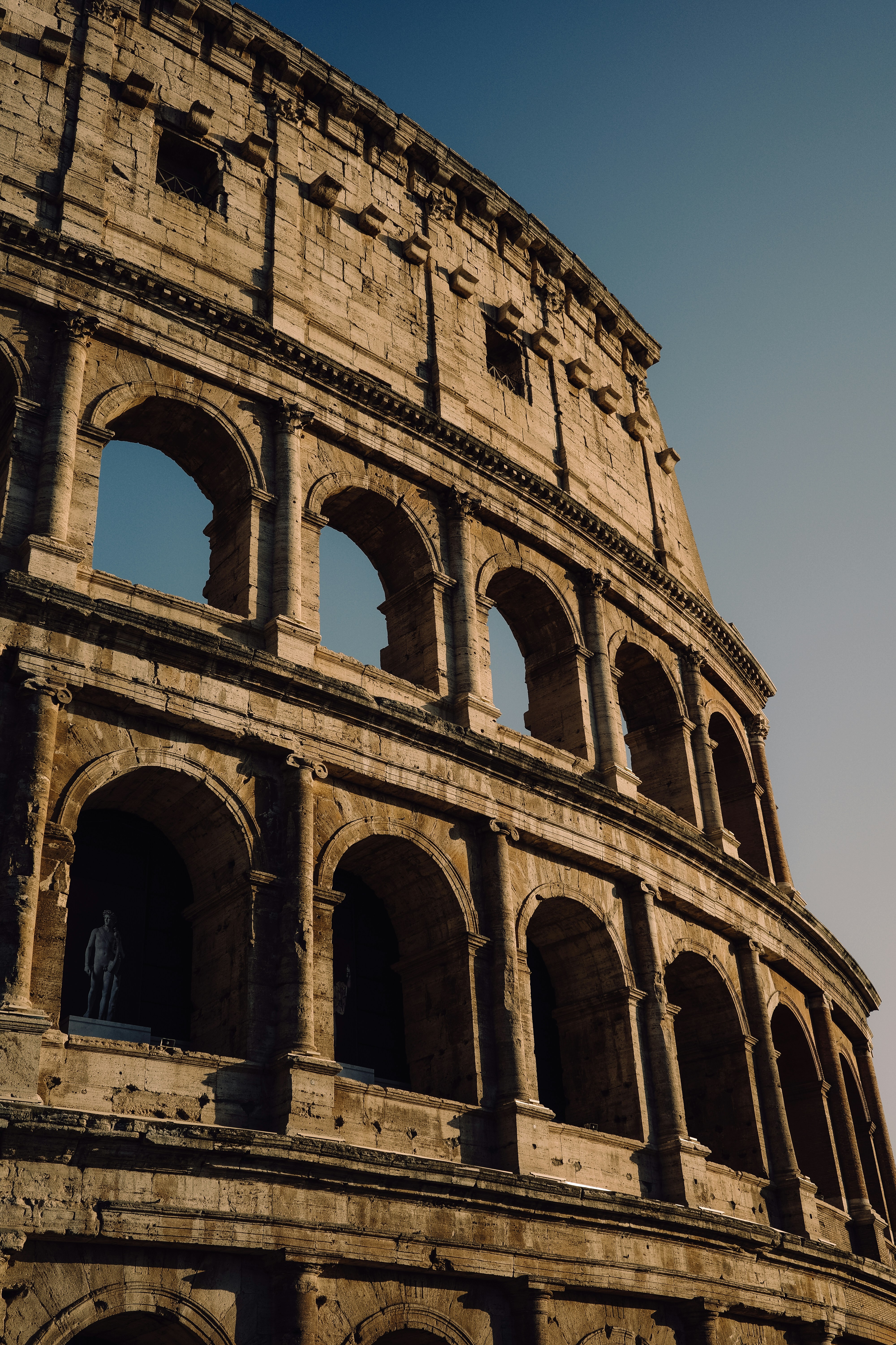 The Colosseum in Rome with stone arches and a statue in an alcove