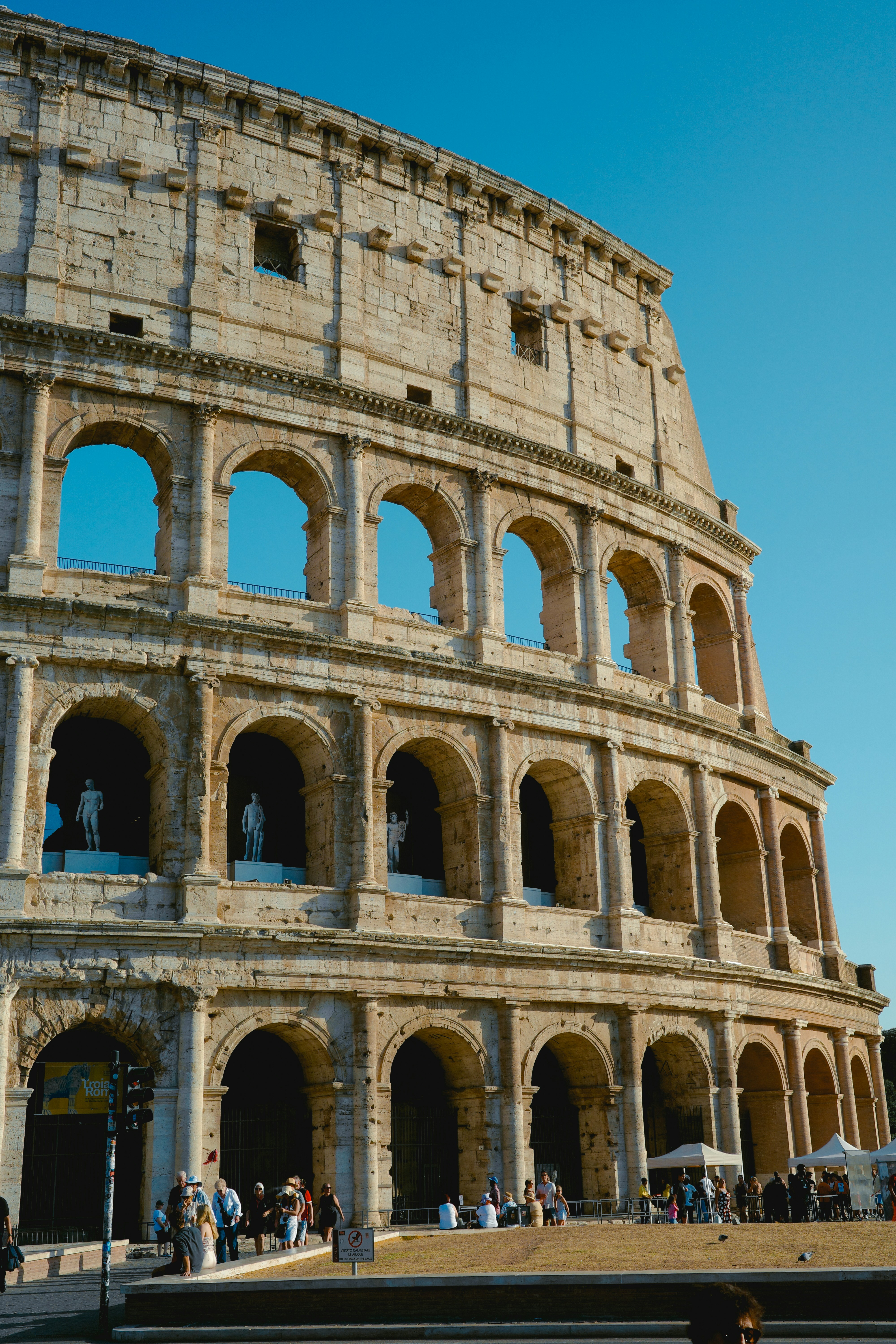 The Colosseum in Rome with stone arches and statues under a clear blue sky