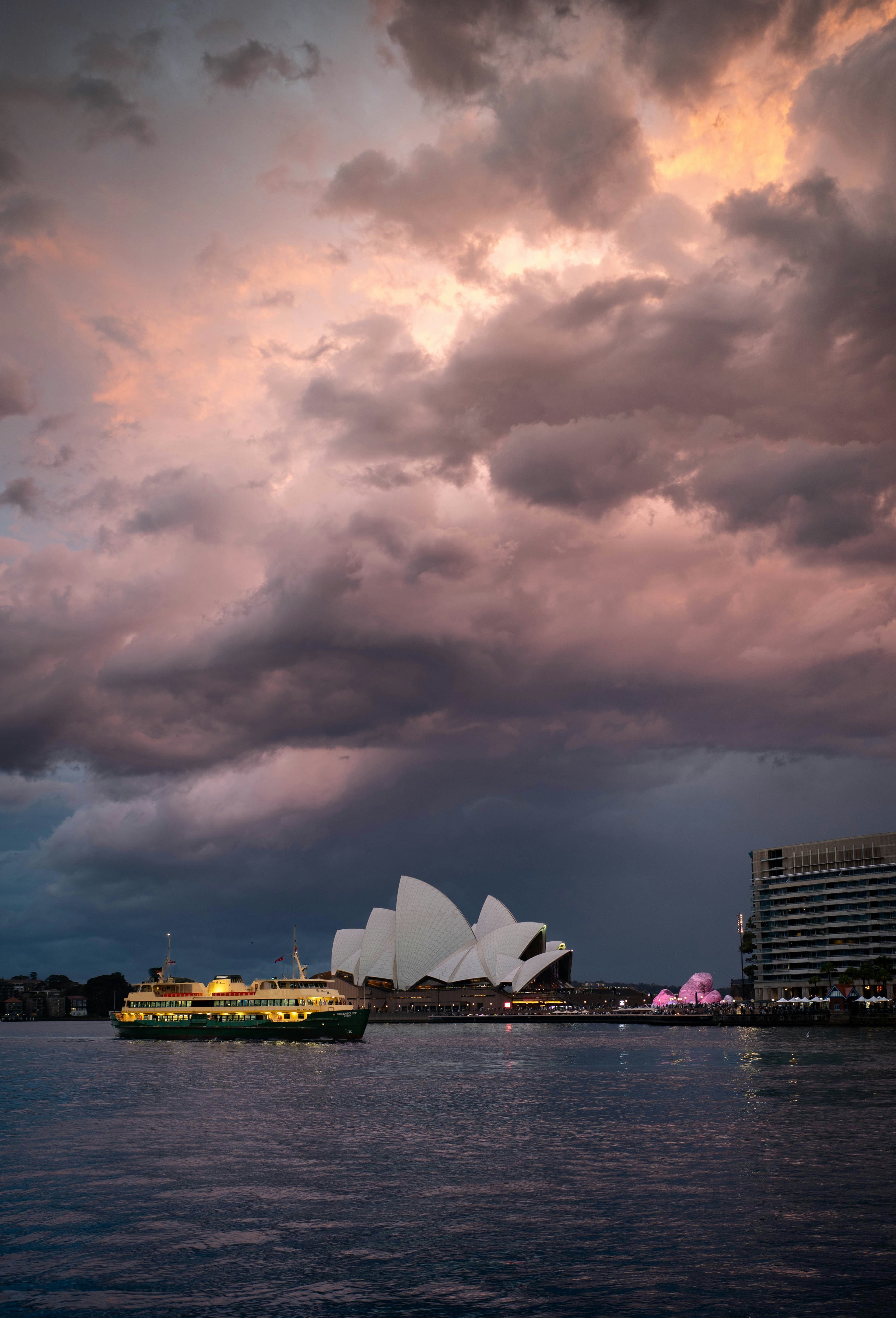 Sebuah feri melewati Sydney Opera House di bawah langit ungu dan oranye yang dramatis