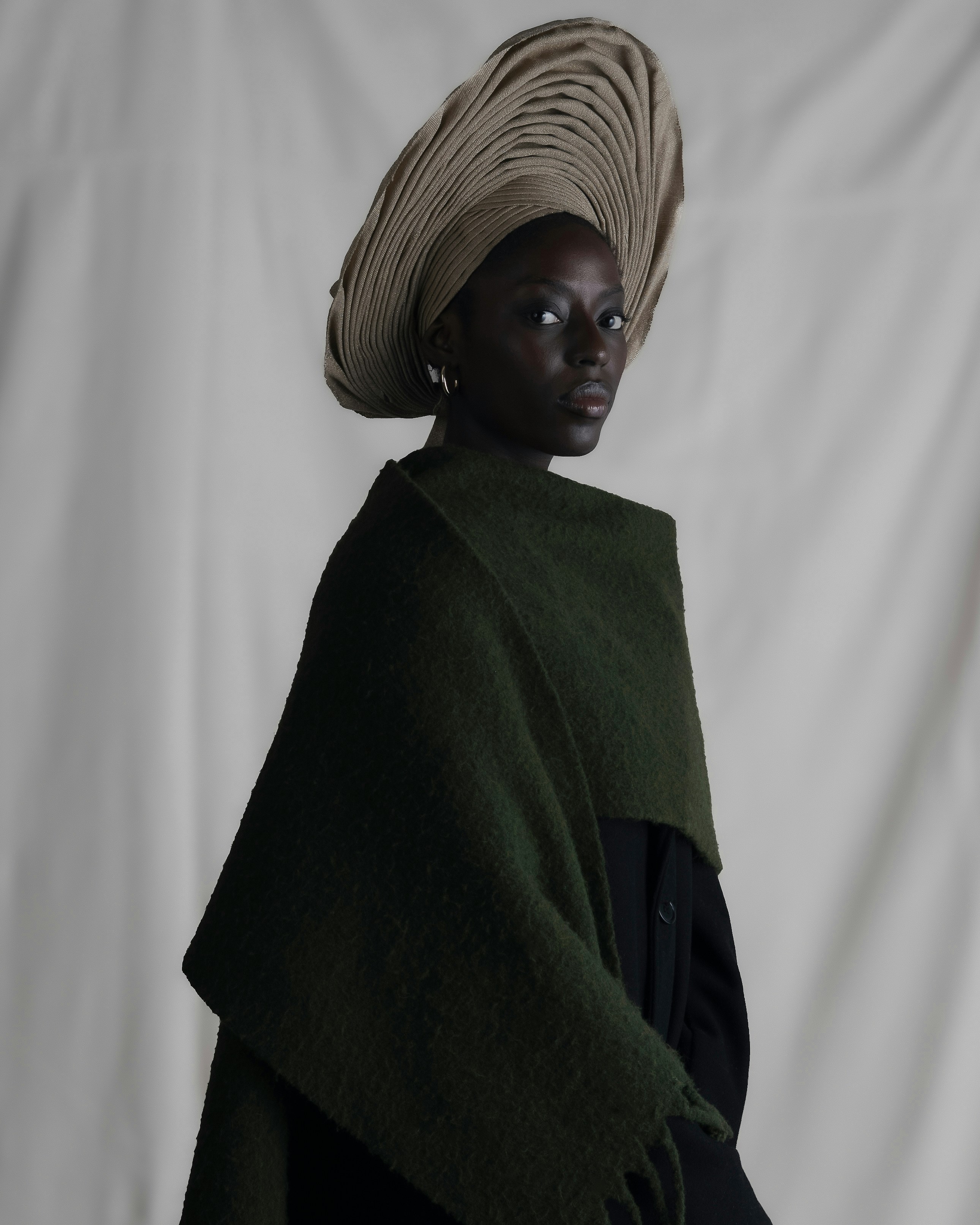 A woman wearing a large pleated beige headwrap and a dark green wool shawl
