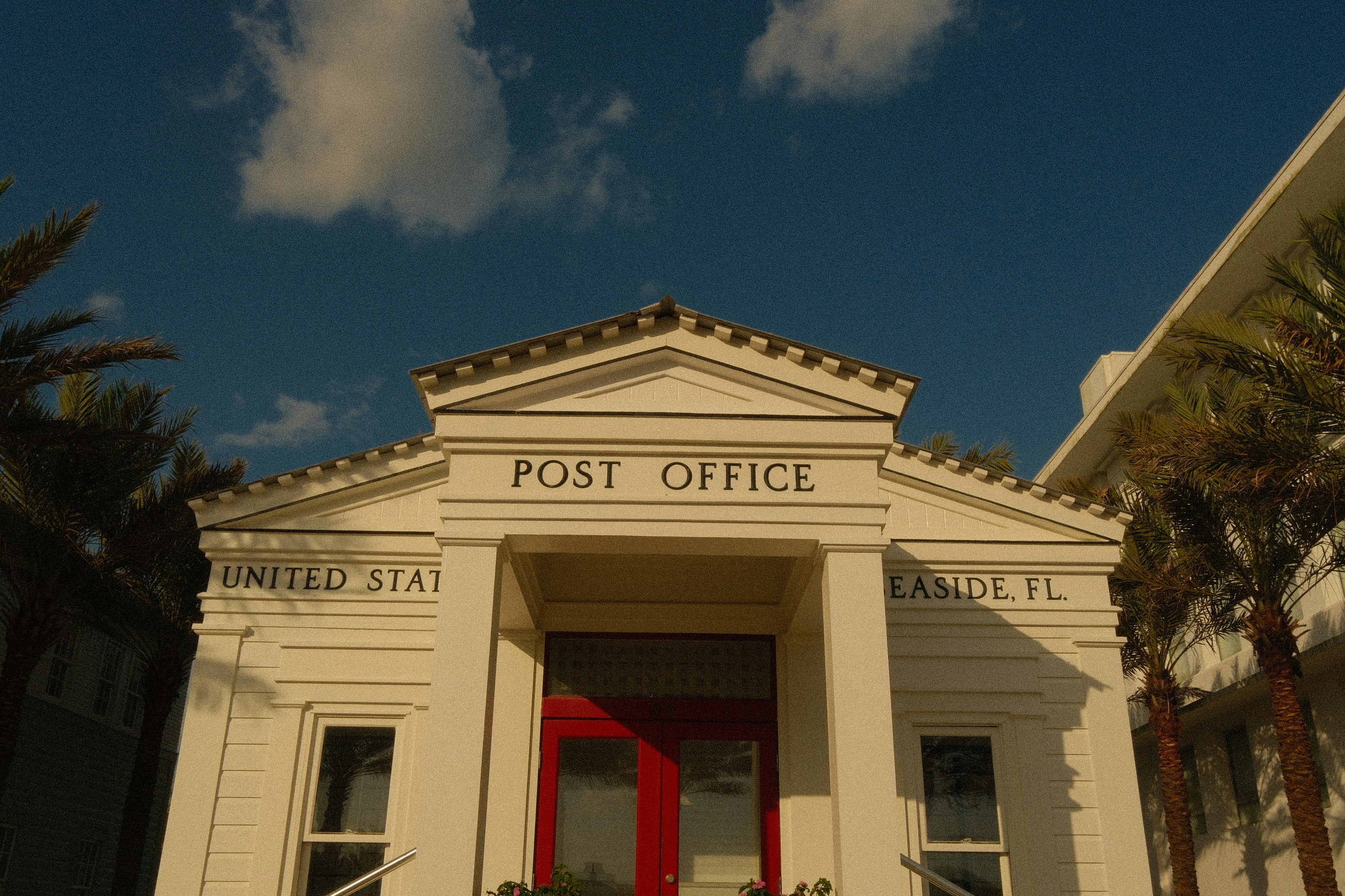 The white post office building in Seaside, Florida, with red doors and palm trees