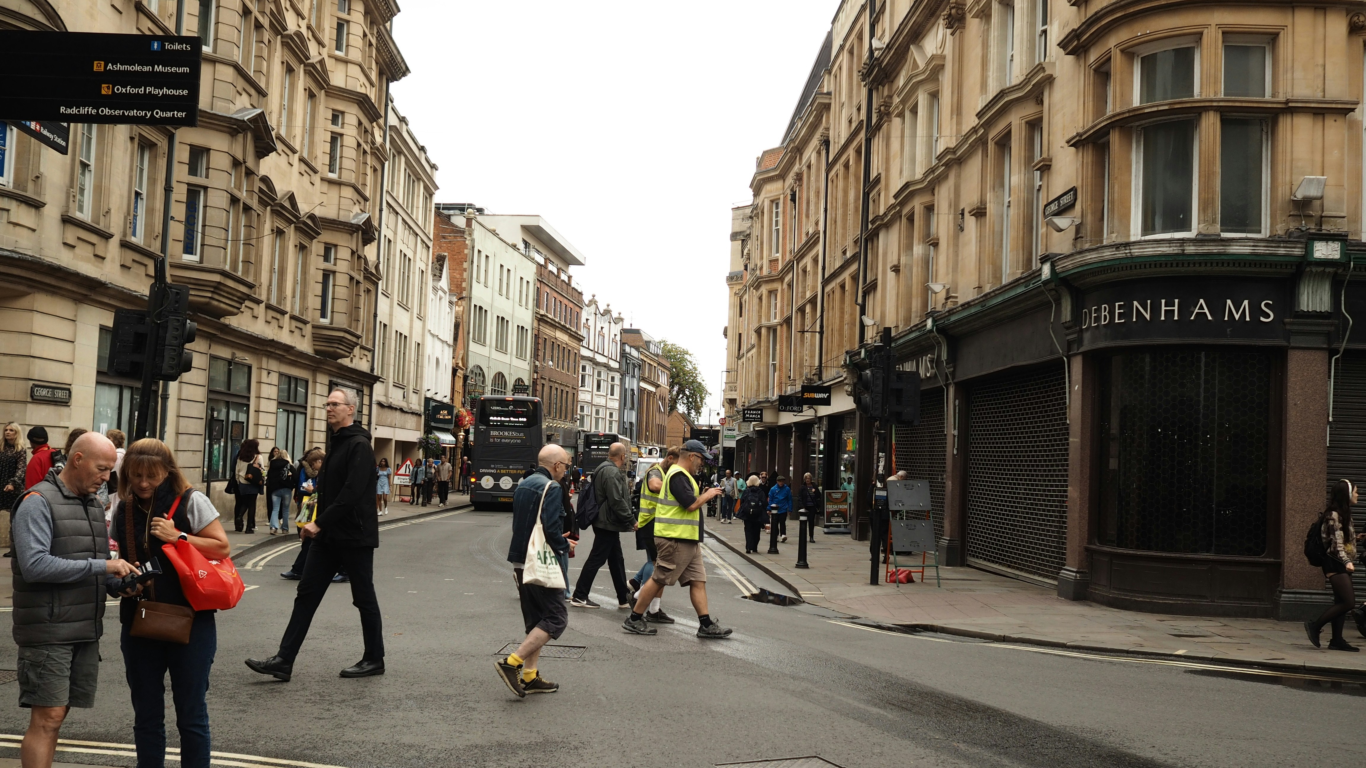 Des gens traversant une rue à Oxford avec des bâtiments historiques en pierre et des boutiques
