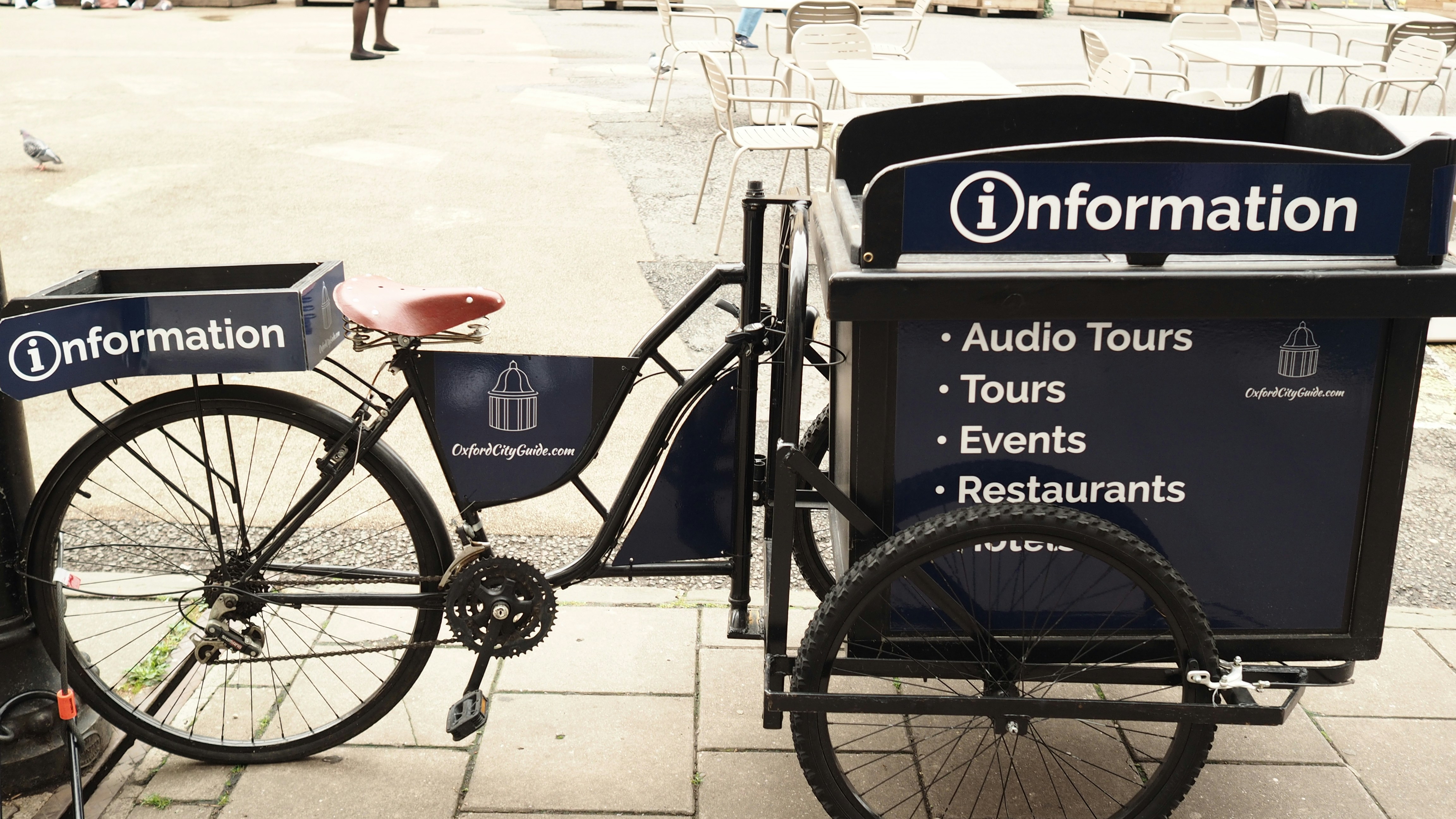 Un vélo cargo noir avec une boîte d’information sur une place pavée de la ville