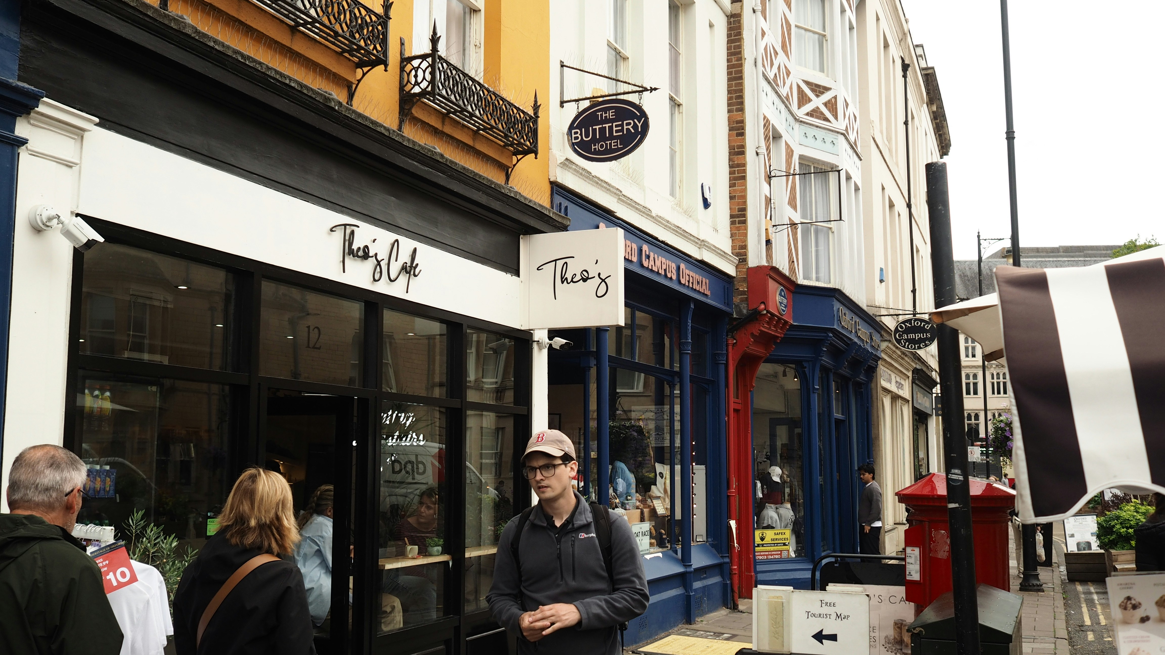 Un homme en casquette de baseball passant devant la devanture d’un café à Oxford