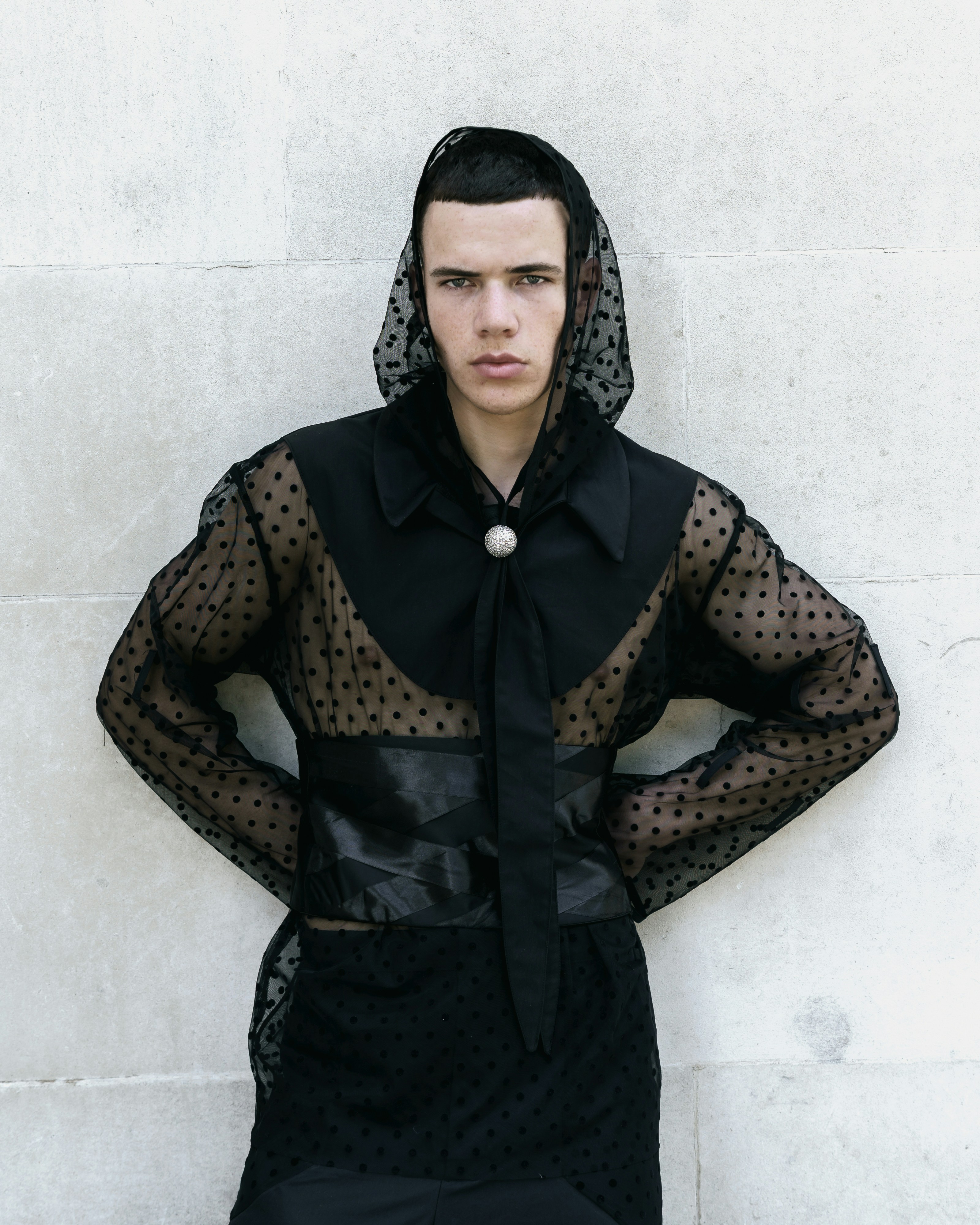 A person wearing a black polka dot mesh hooded shirt and satin waist wrap