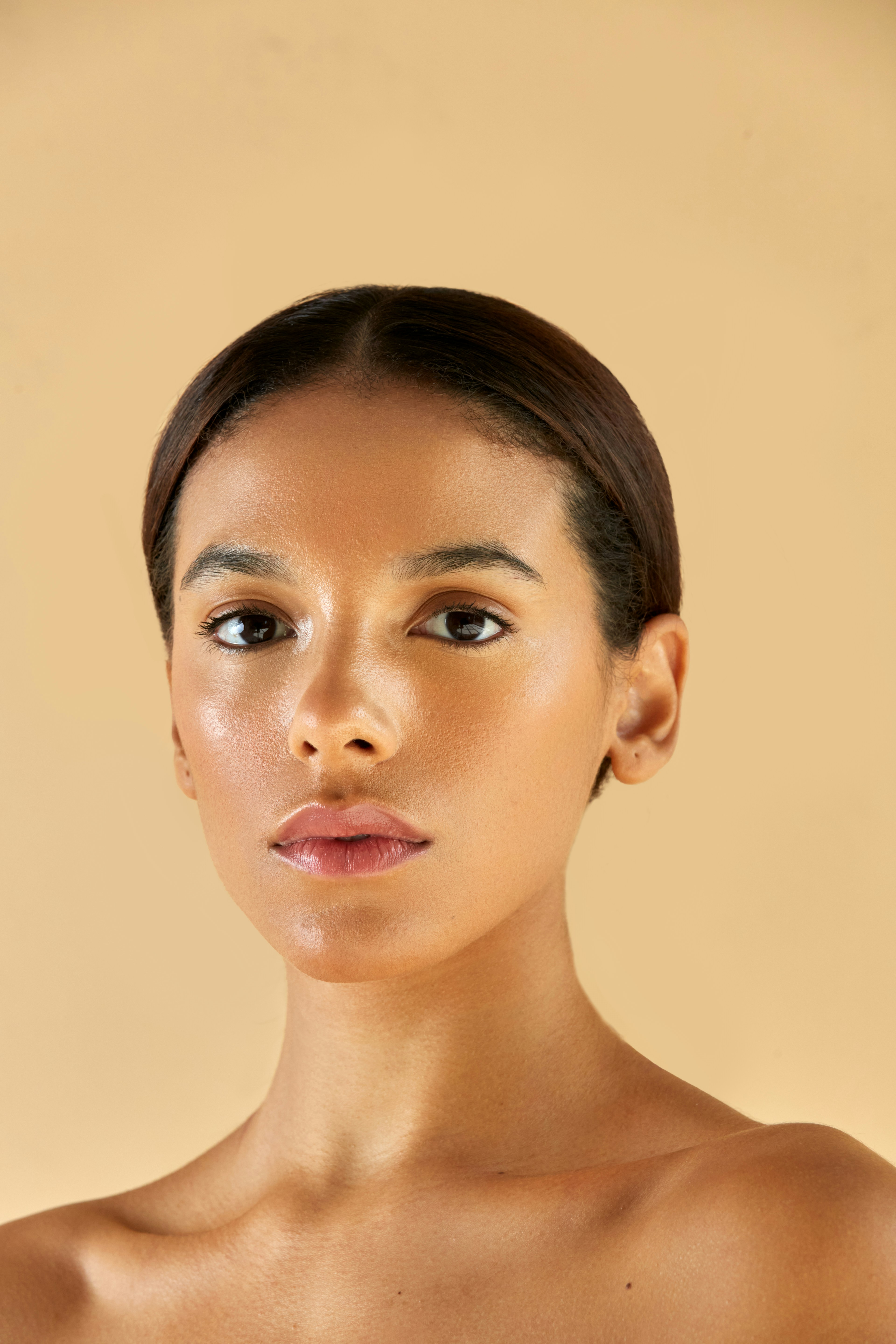 A woman with dark hair pulled back against a plain beige background