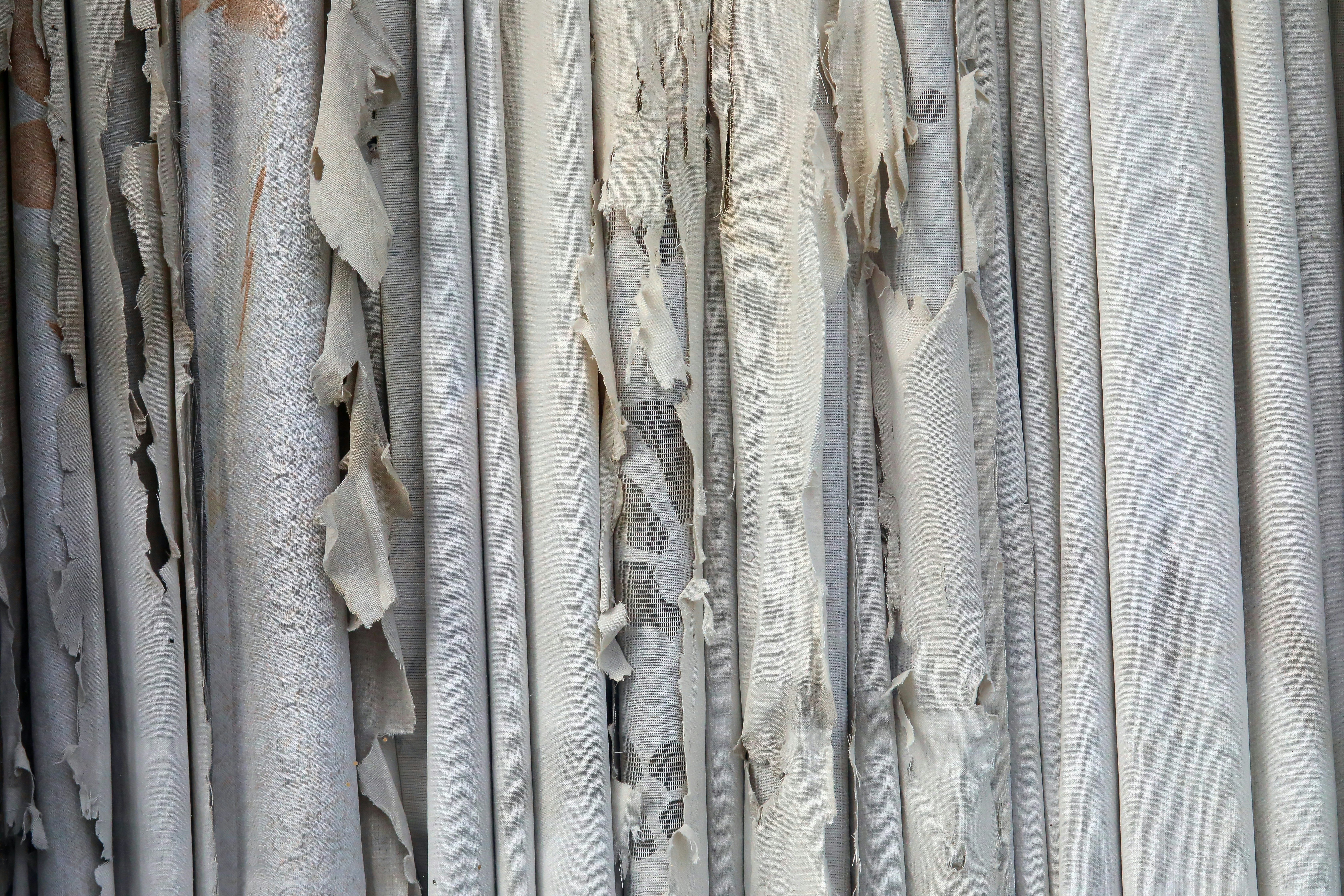 Vertical strips of tattered off-white fabric hanging in overlapping layers