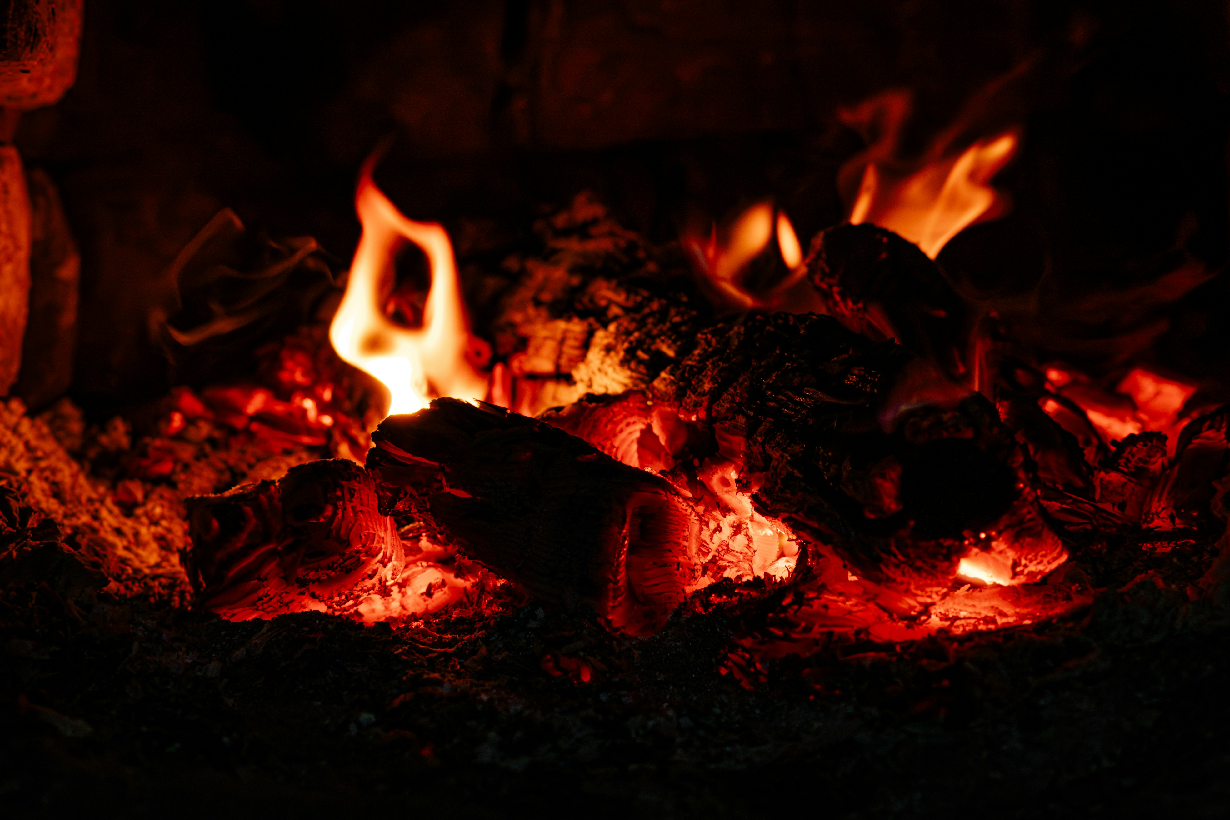 Des flammes orange vif vacillant au-dessus de braises rouges et de bûches de bois calcinées