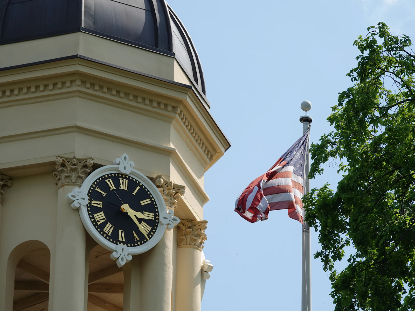 A university clock tower with Roman numerals beside an American flag