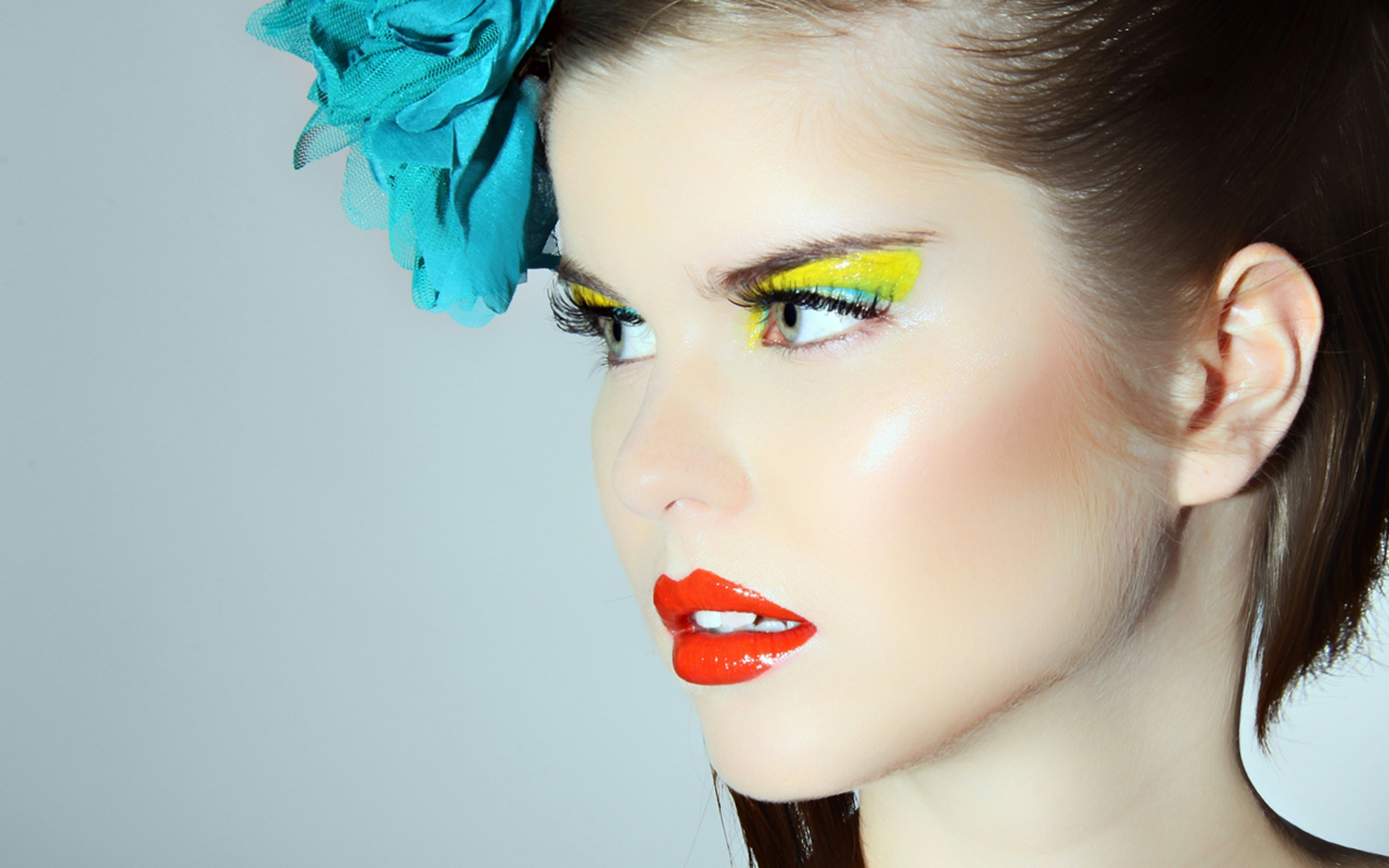 A woman with bright yellow eyeshadow and red lipstick wearing a teal hair flower
