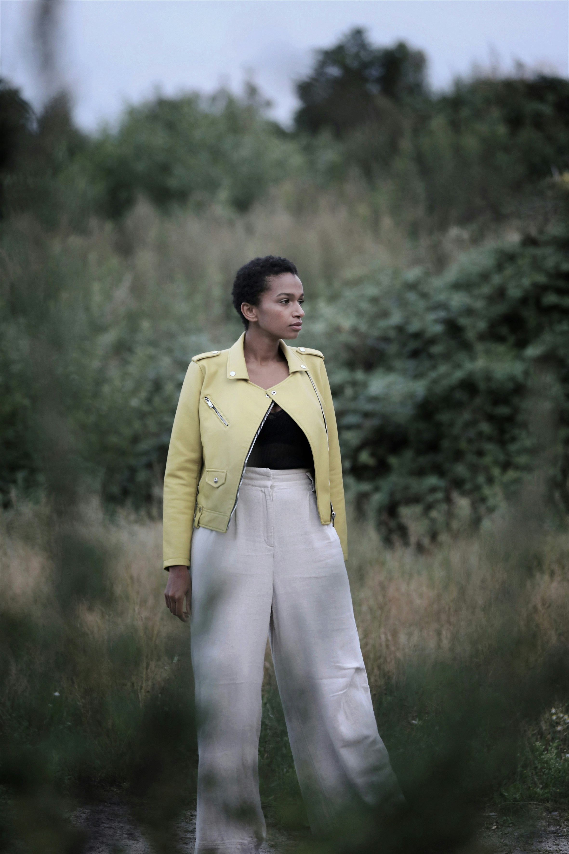 A woman in a yellow leather jacket and white trousers in a field