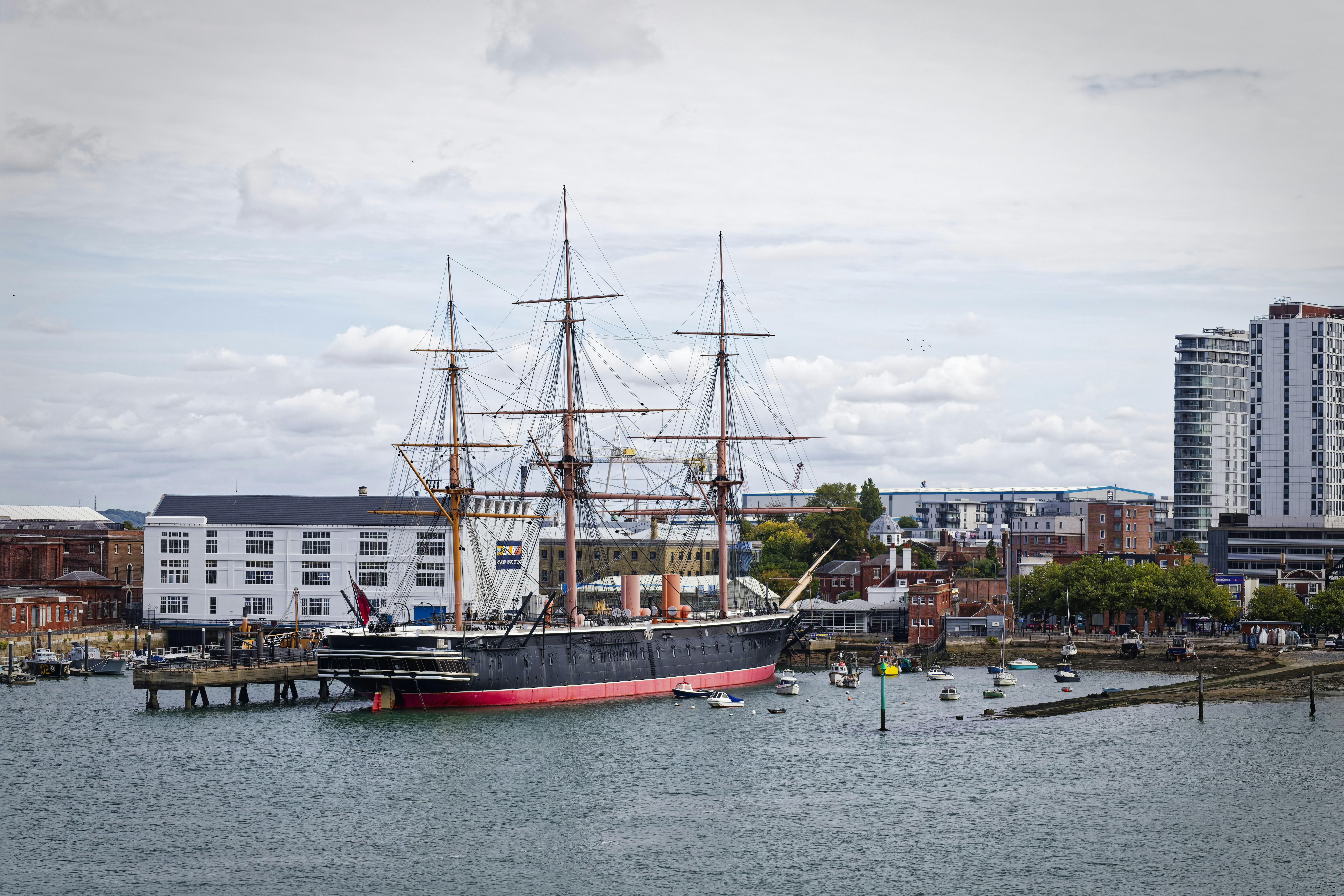 Black and white view of HMS Warrior moored at Portsmouth Historic Dockyard, with modern towers behind