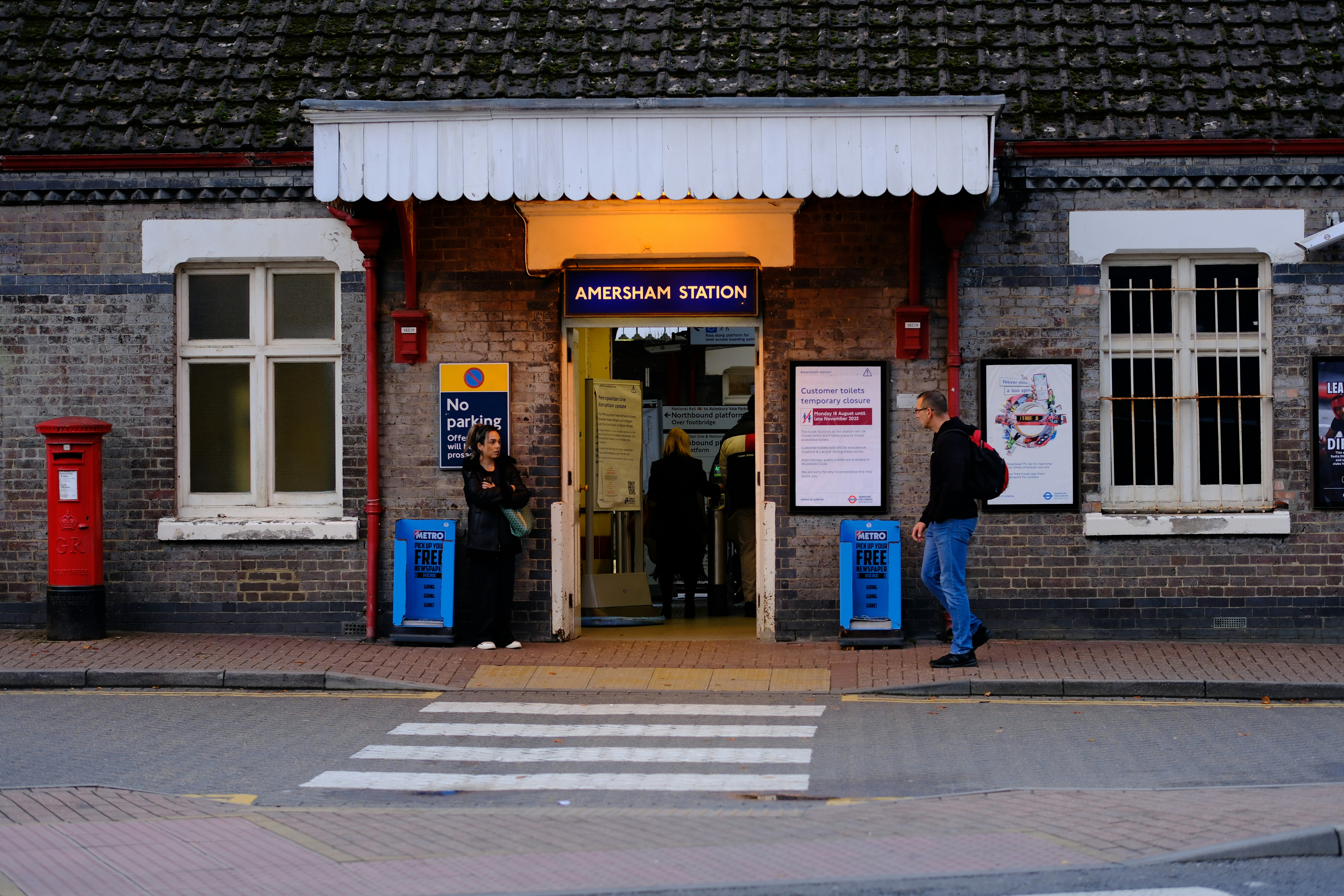 People entering Amersham Station through a brick building with a red post box