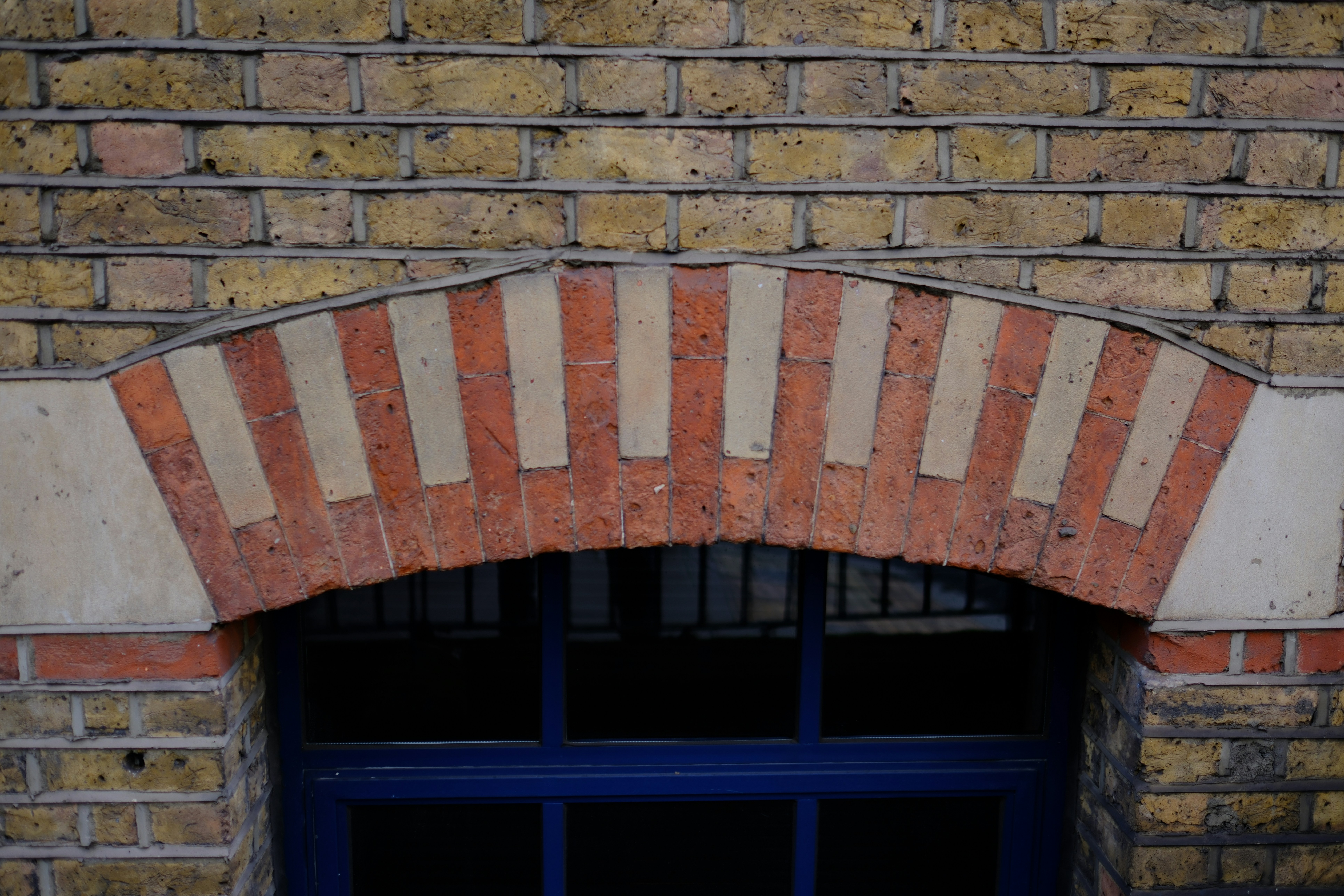 An arched window with alternating red and light stone bricks in a brick wall