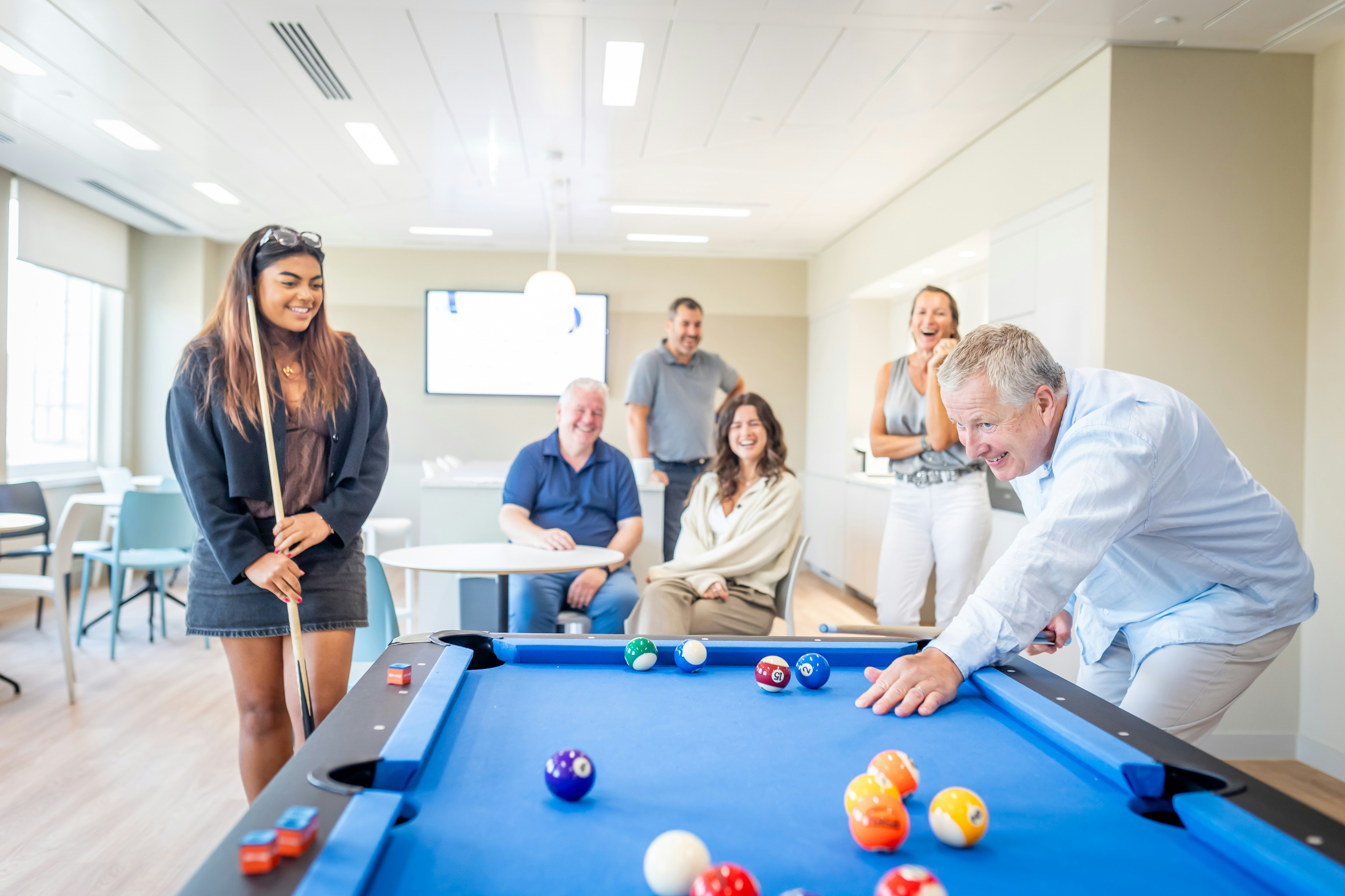 Eine Gruppe von Leuten spielt Billard in einem hellen Büro-Pausenraum