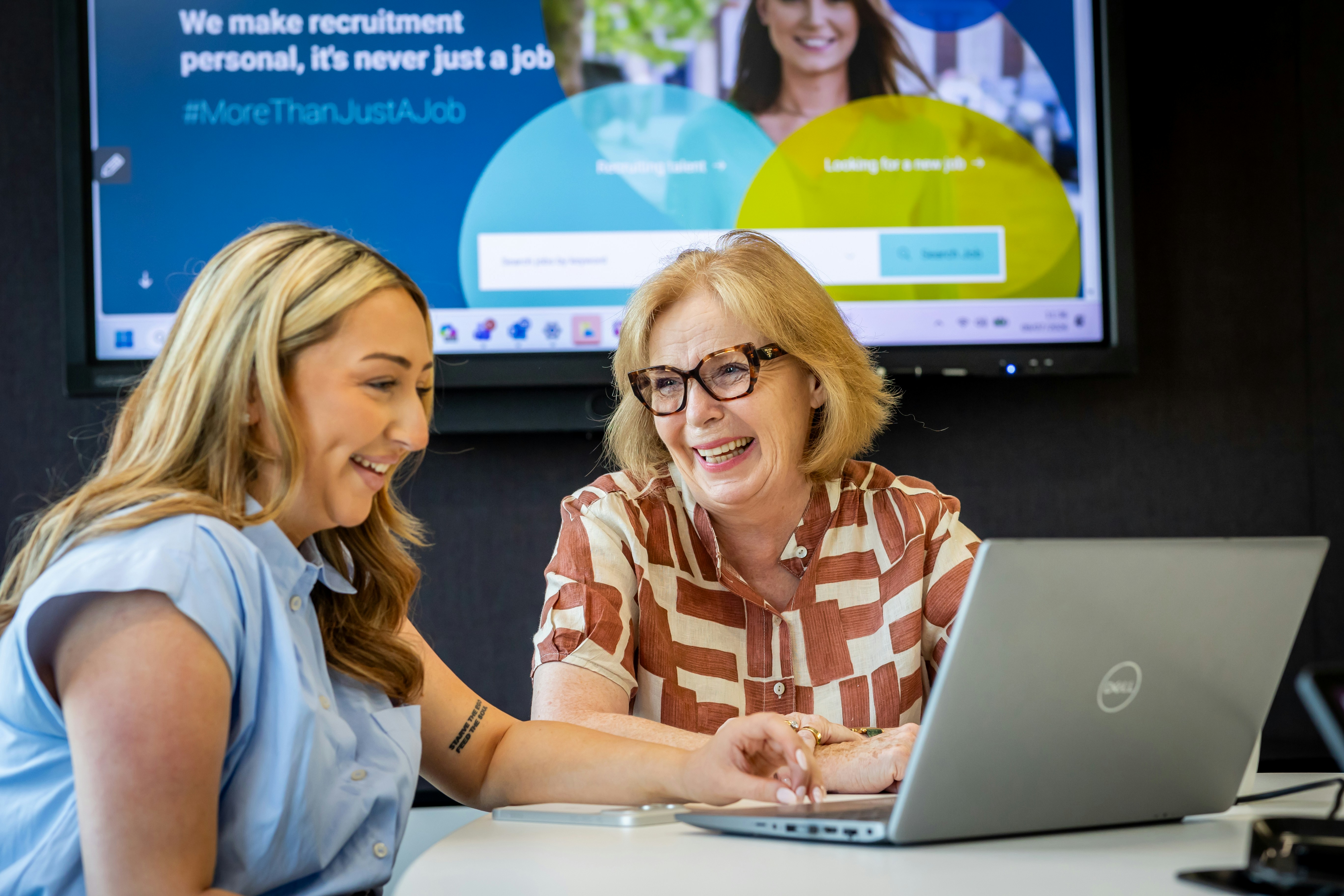 Zwei Frauen, die auf einen Laptop-Bildschirm in einem modernen Bürobereich schauen