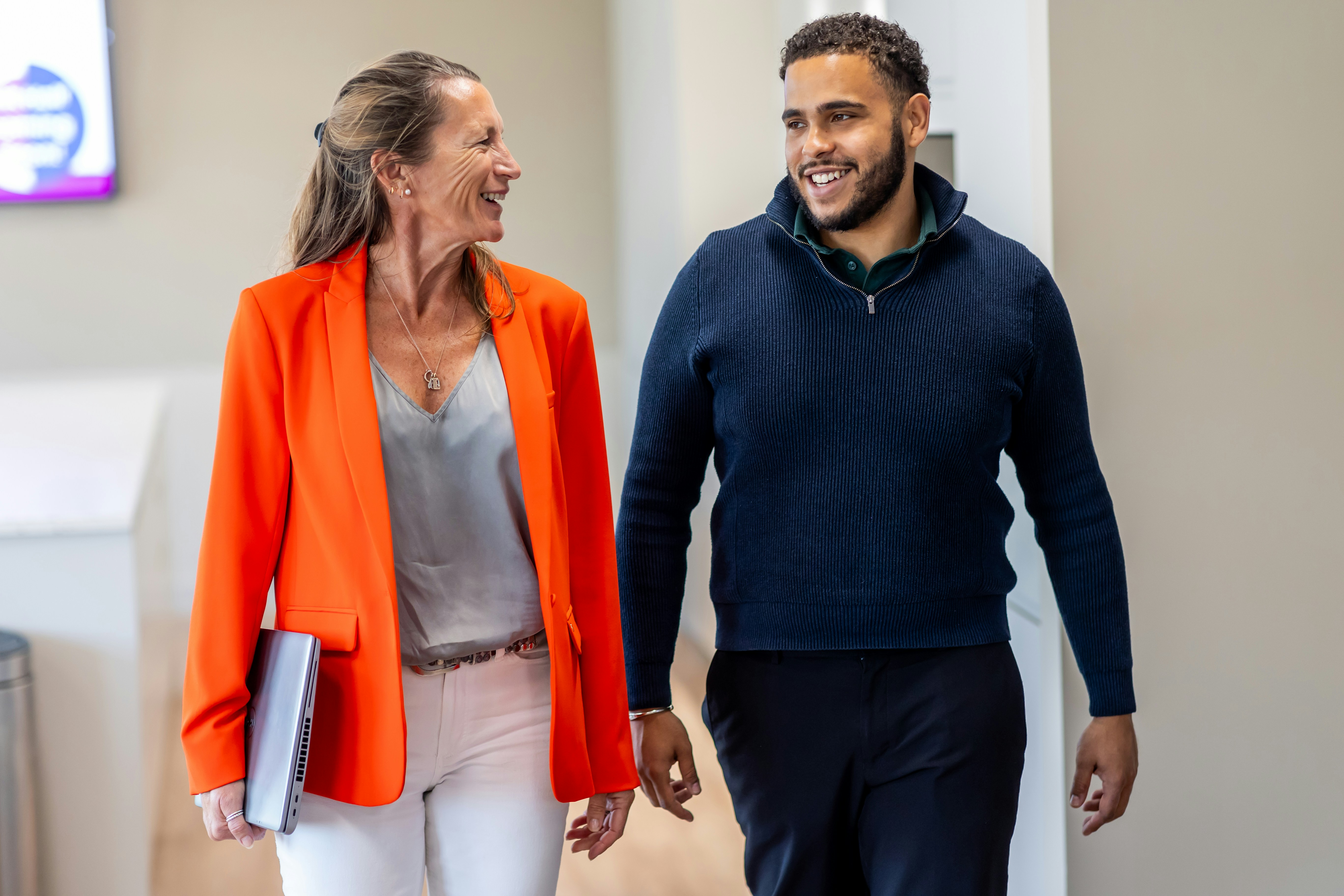 A woman in an orange blazer and a man in a navy sweater walking