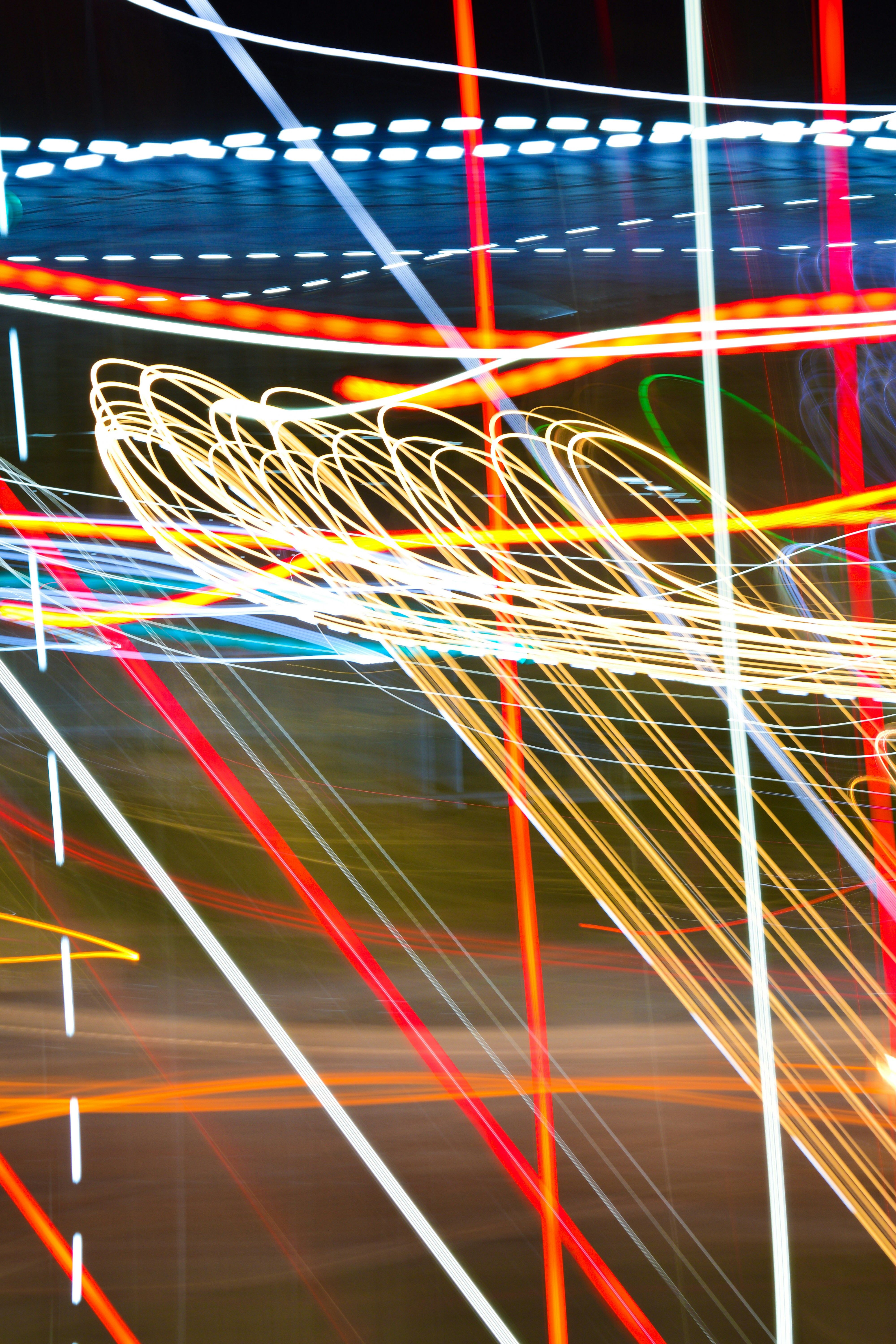 Long exposure light trails in red, white, and yellow against a dark background