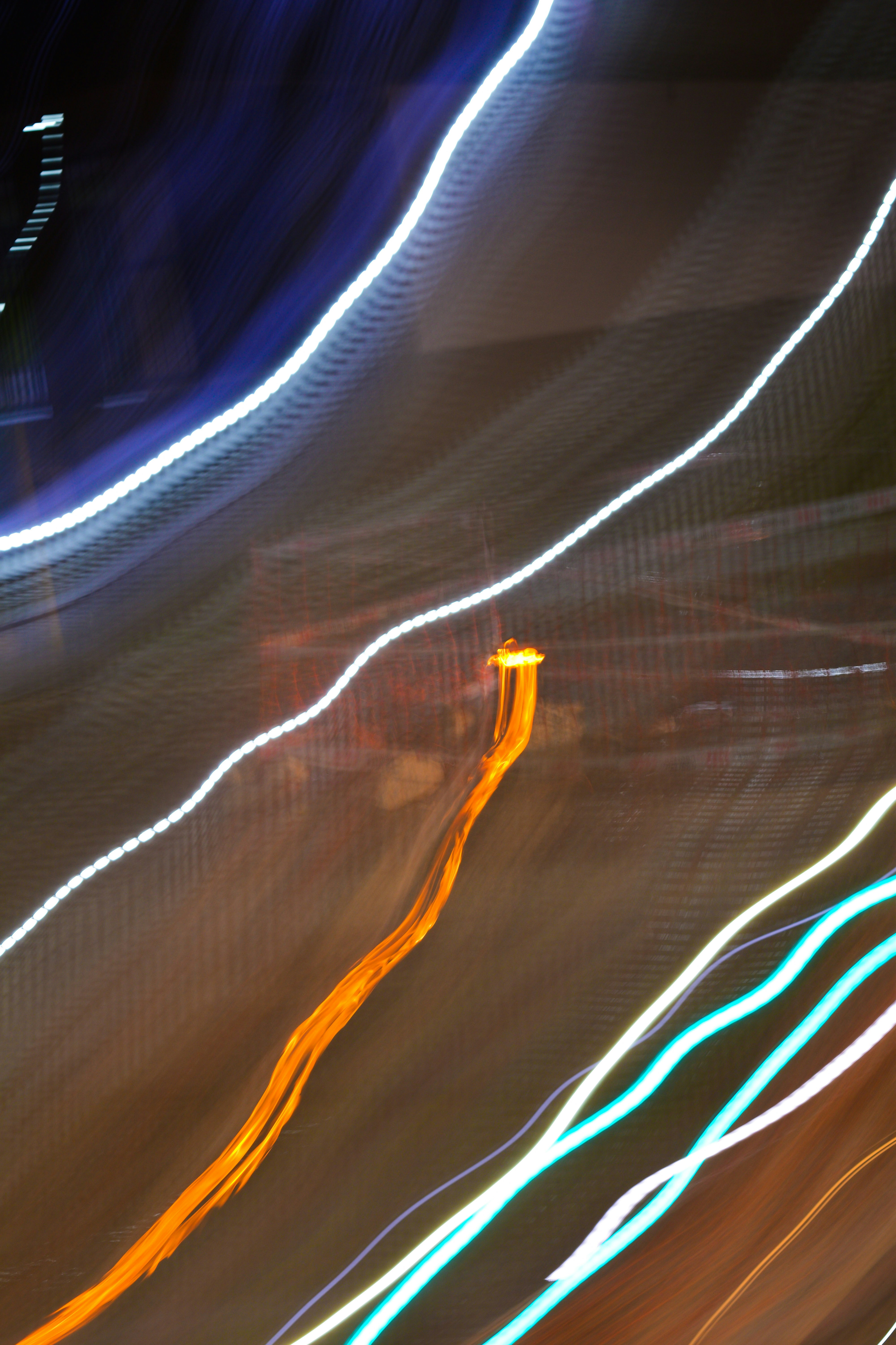 Long exposure light trails in white, orange, and cyan against a dark background
