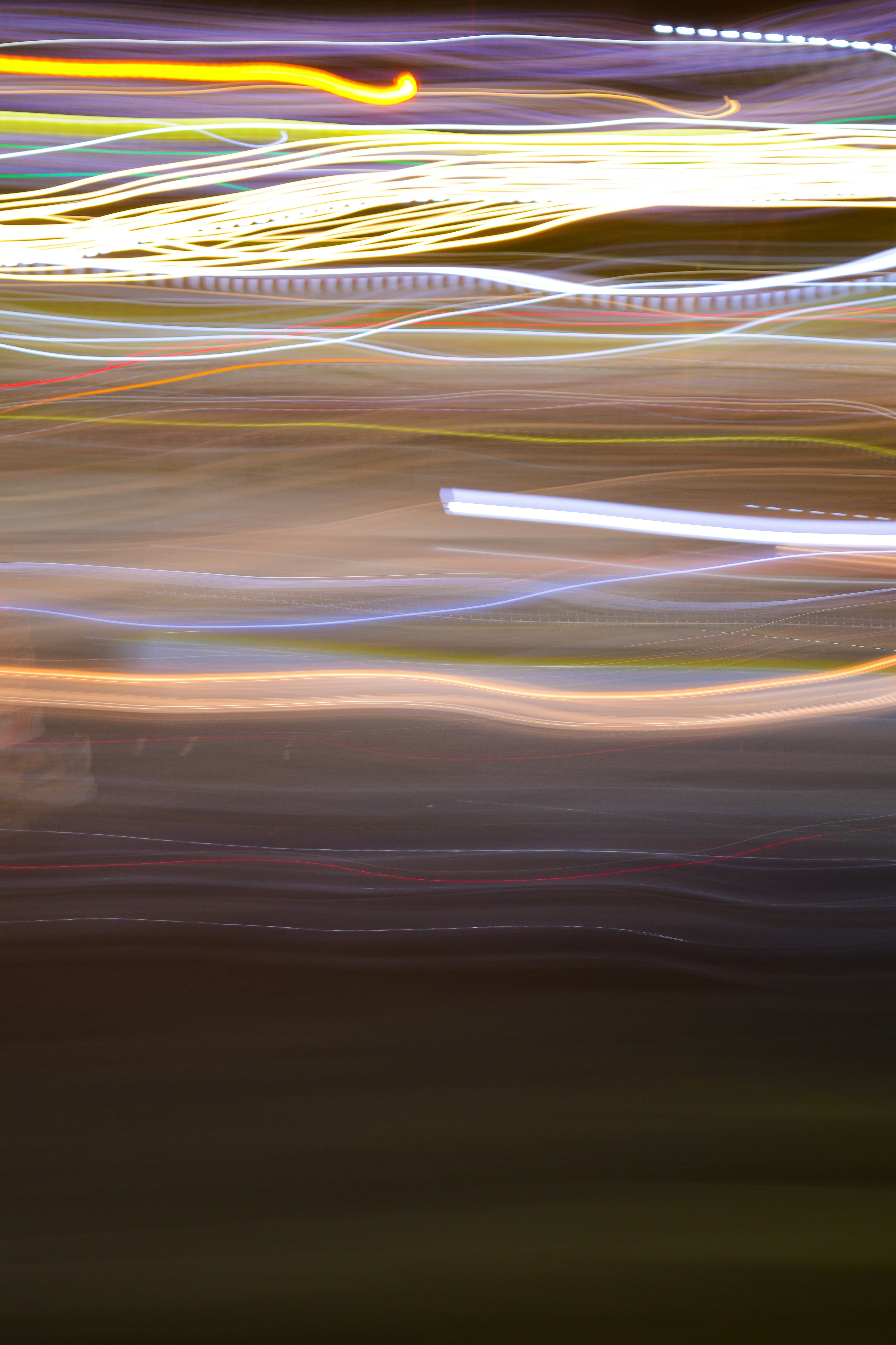 Long exposure light trails in yellow, white, and orange across a dark background