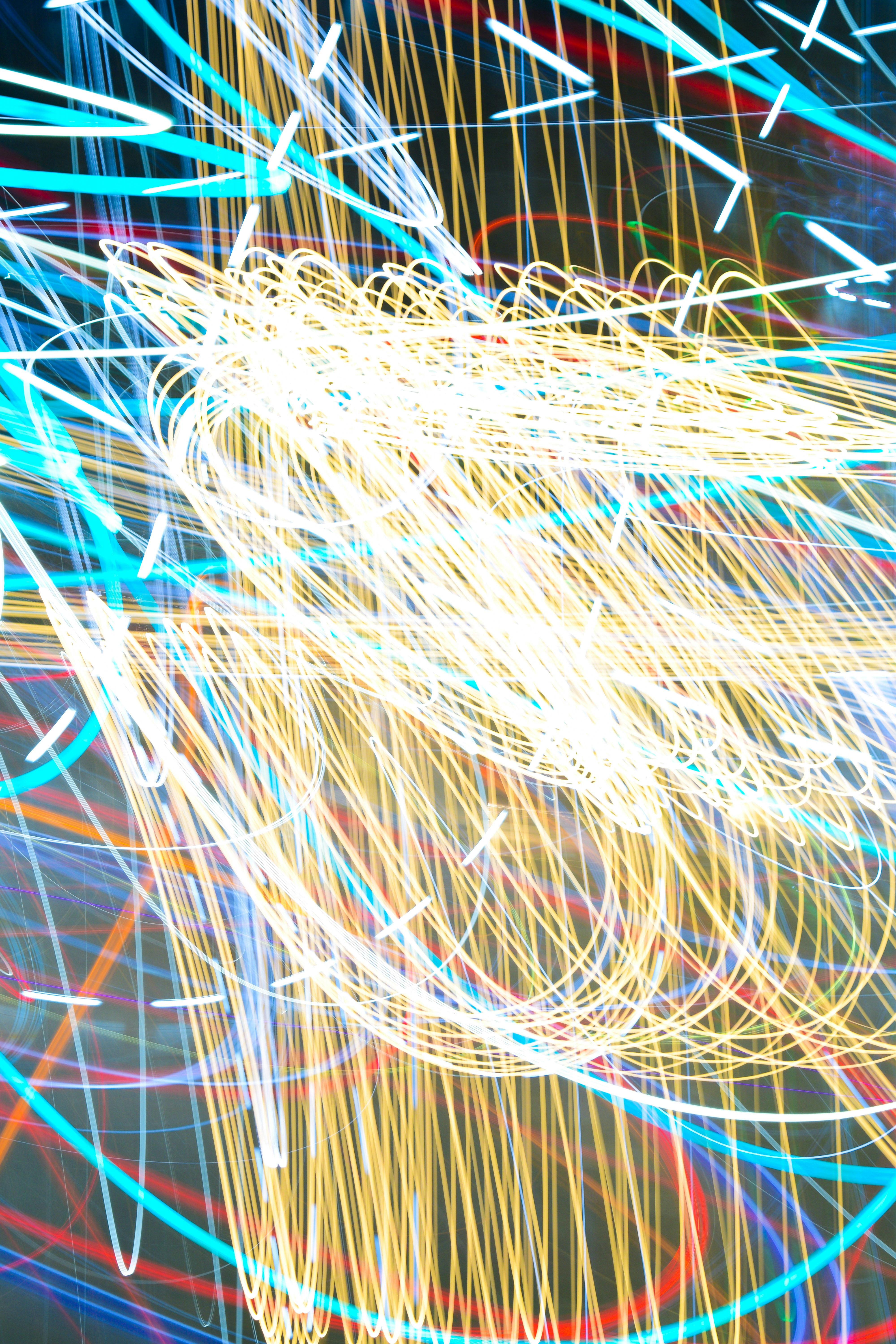 Long exposure light trails in vibrant yellow, blue, and red against a dark background