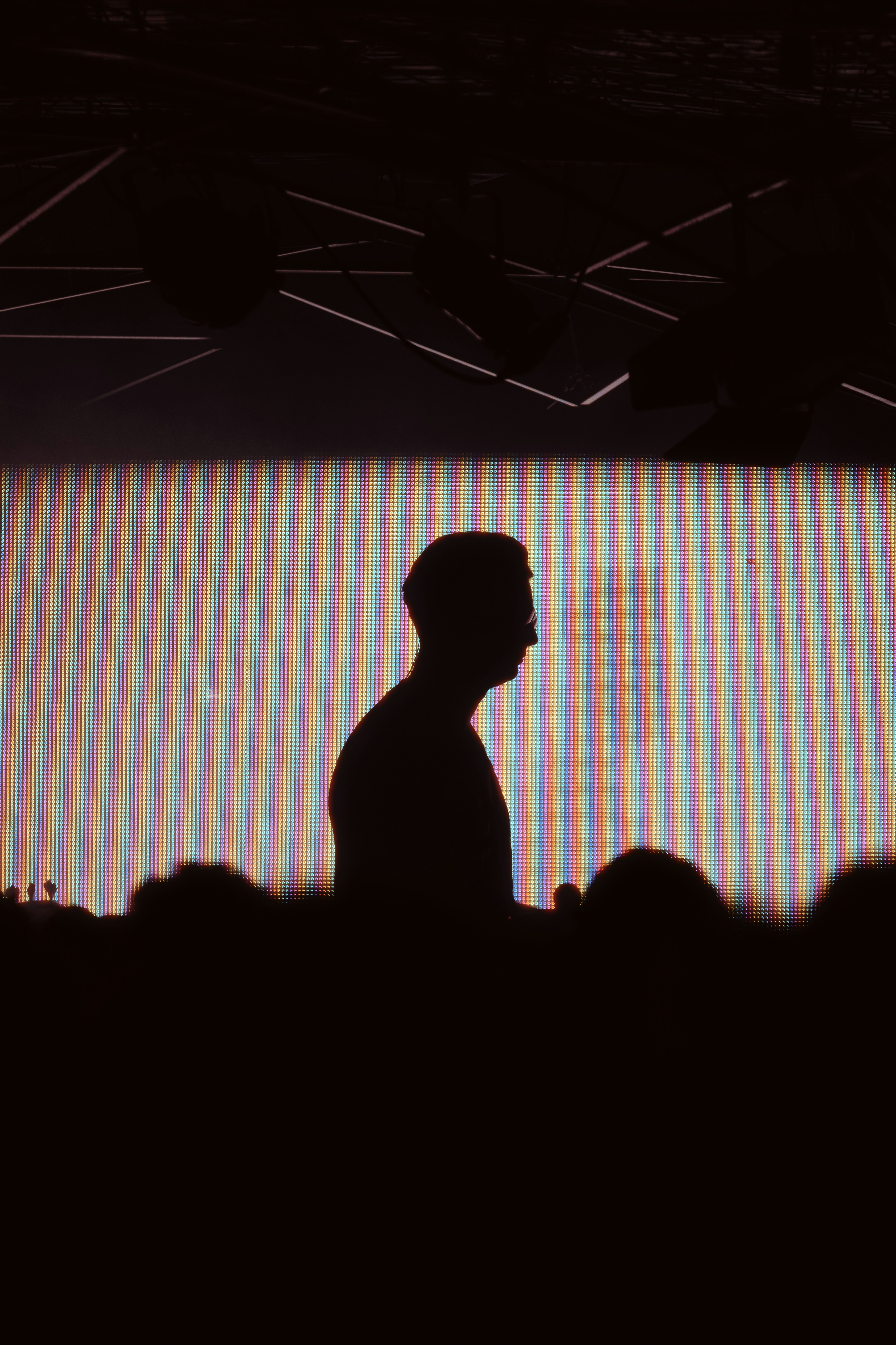 A person in silhouette against a bright screen with vertical rainbow stripes