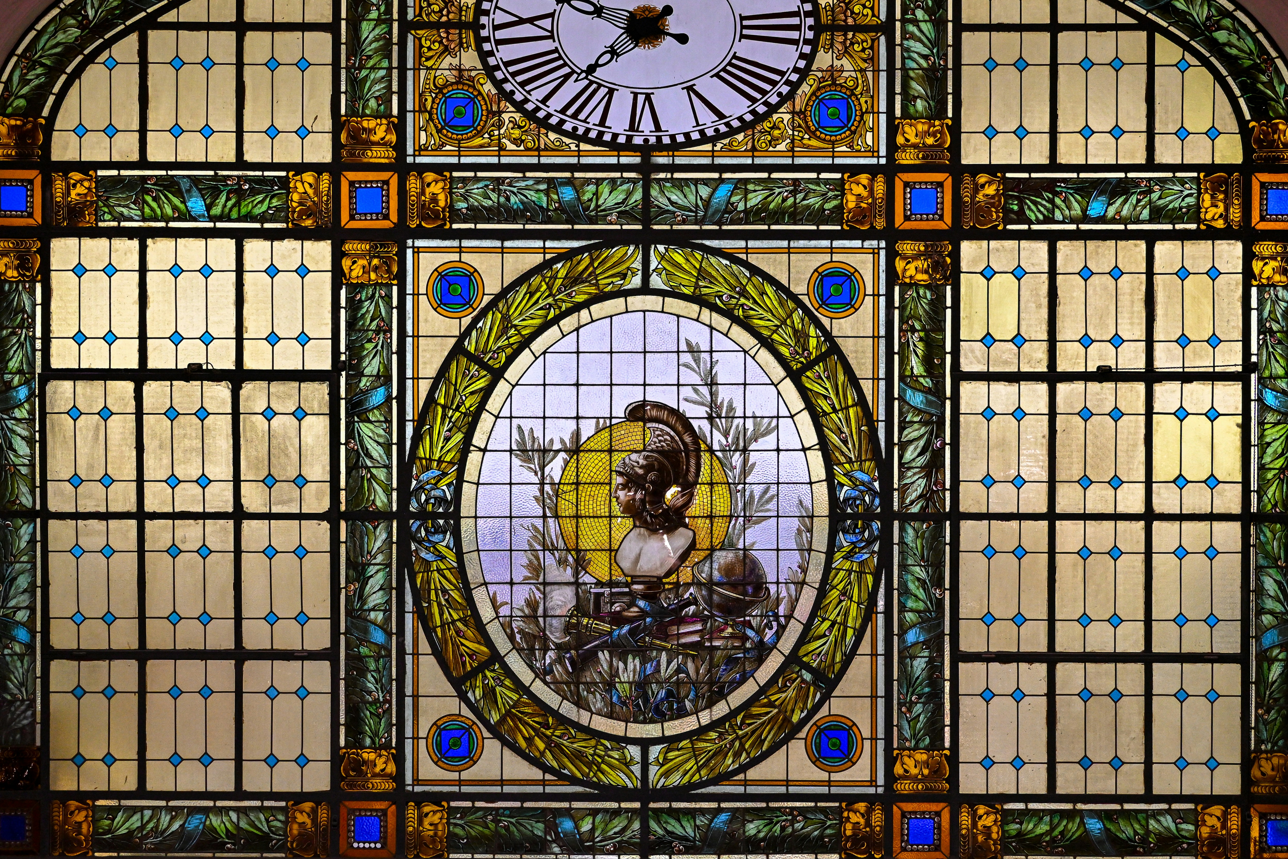 Stained glass window featuring a classical helmeted bust and a clock face