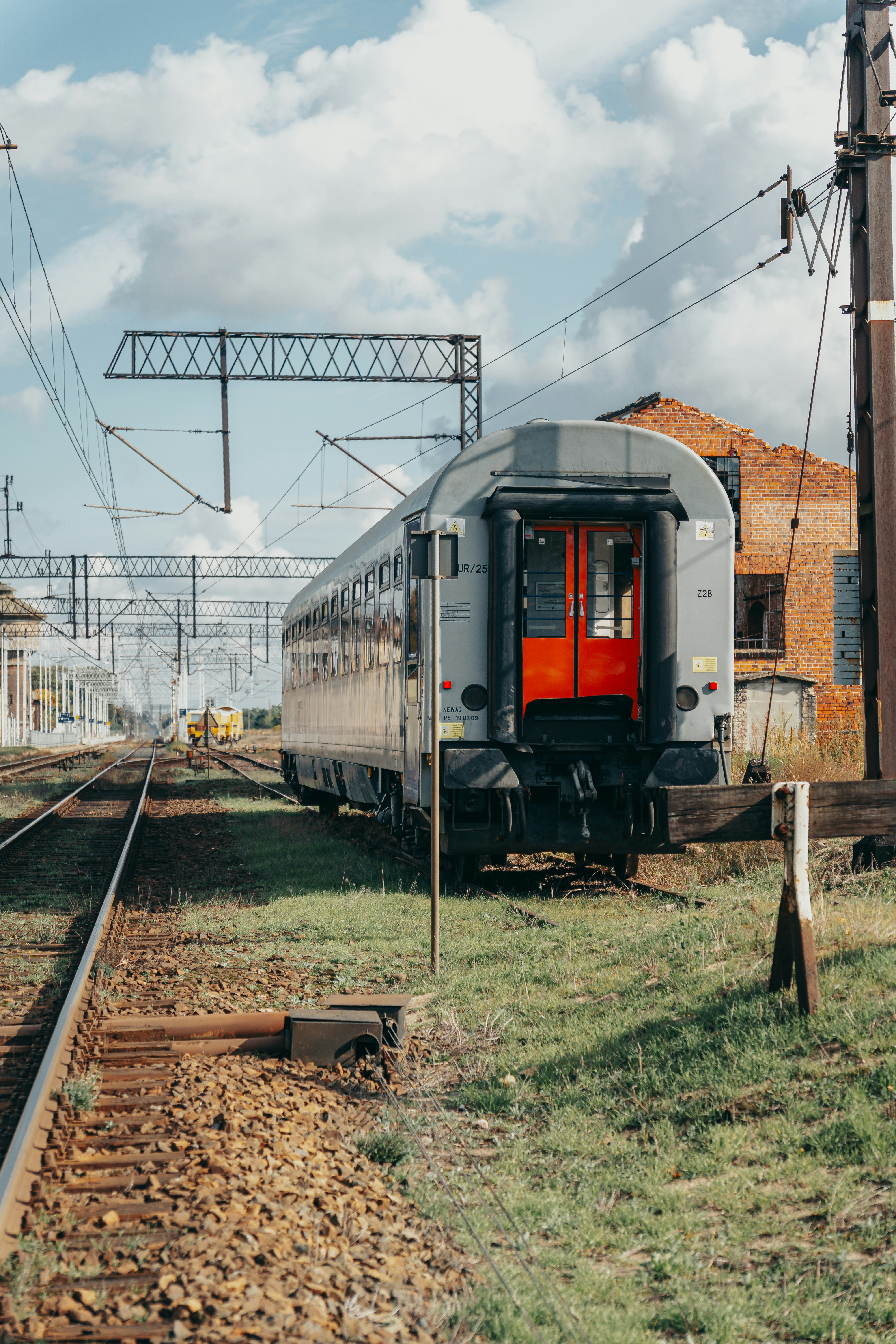 Um vagão de trem de passageiros cinza com portas laranja brilhante em uma linha férrea