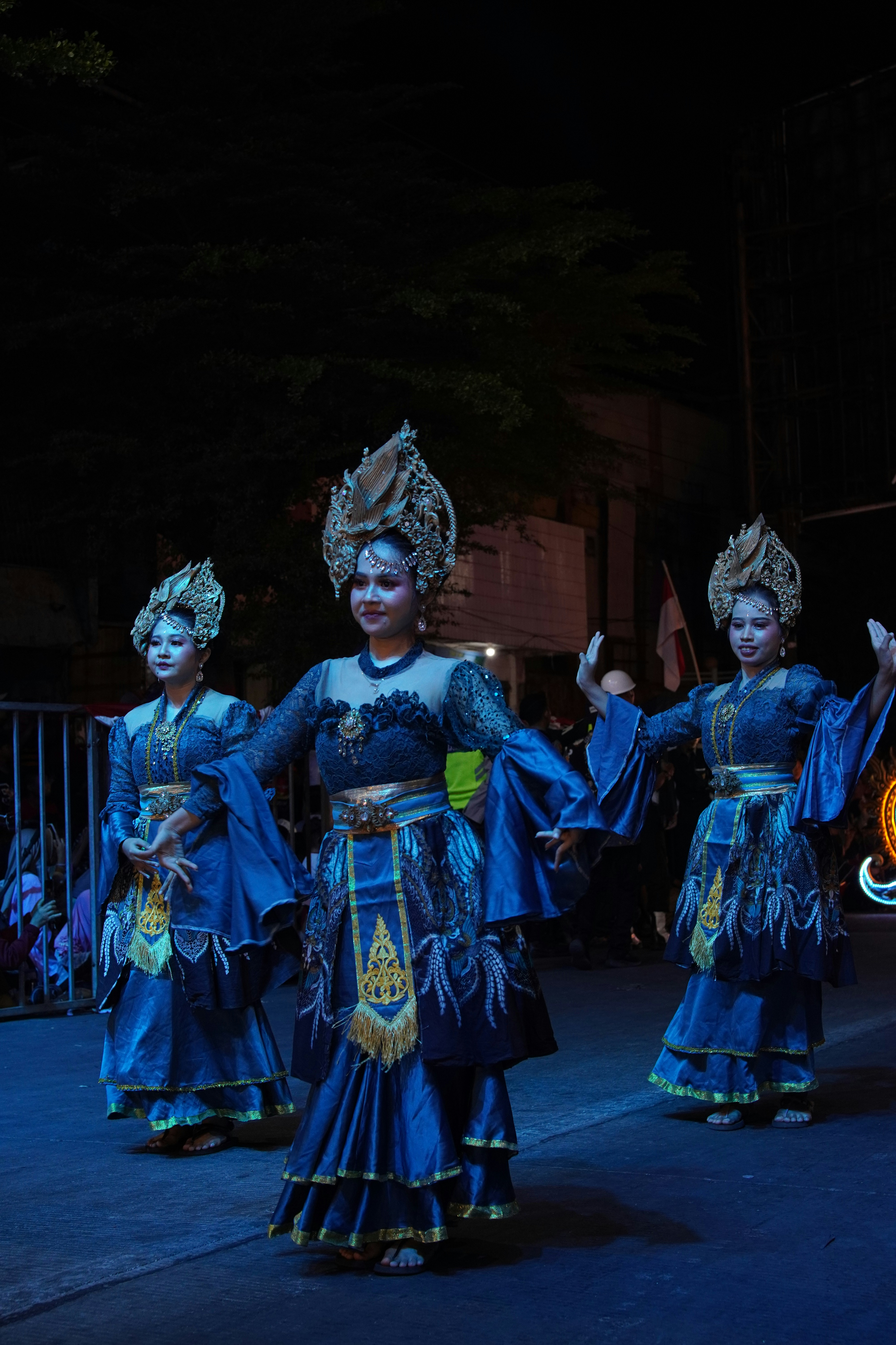 Tres personas con ornamentados trajes tradicionales azules y tocados dorados interpretando un baile al aire libre