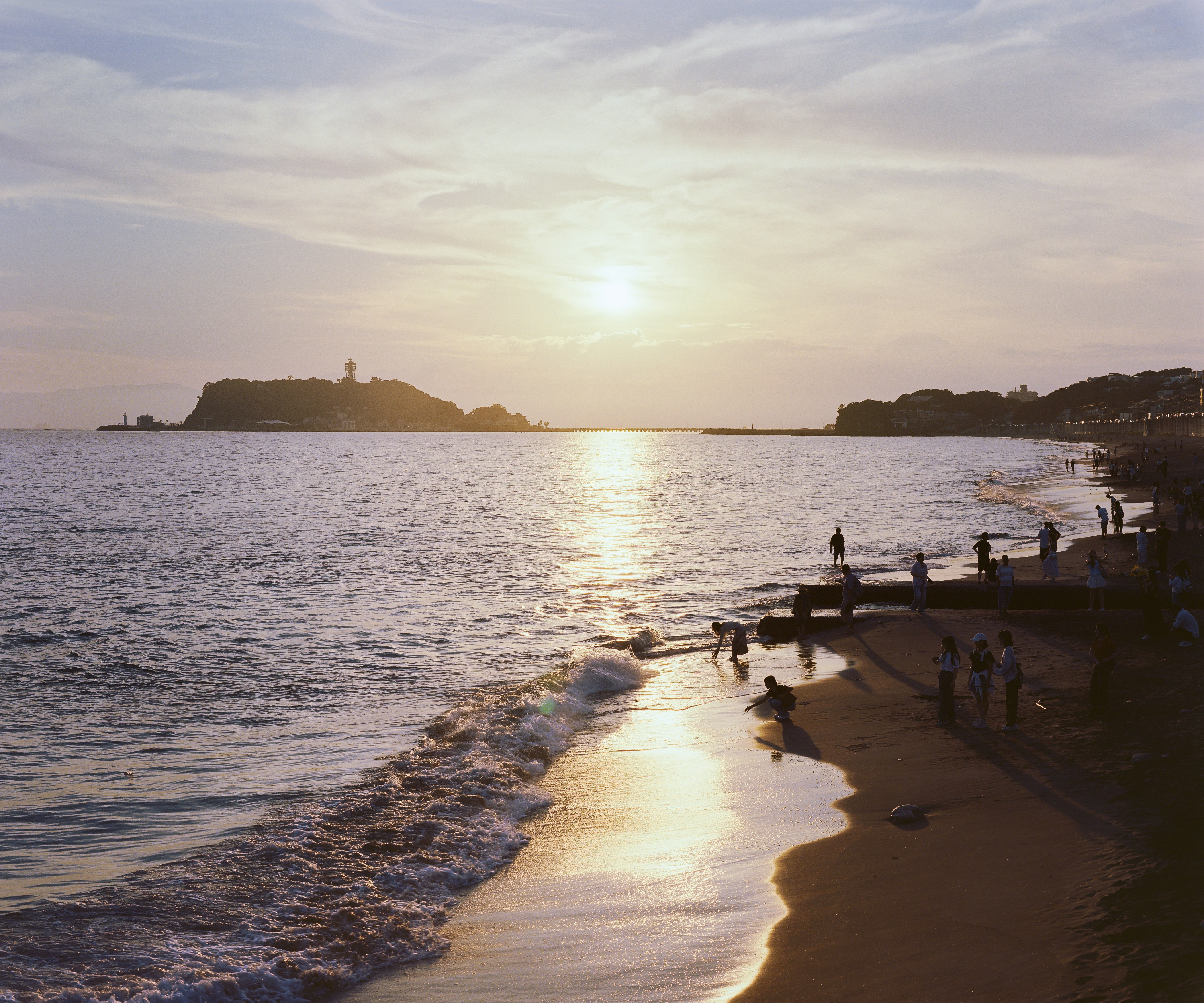 People on a sandy beach at low sun with Enoshima island in the distance