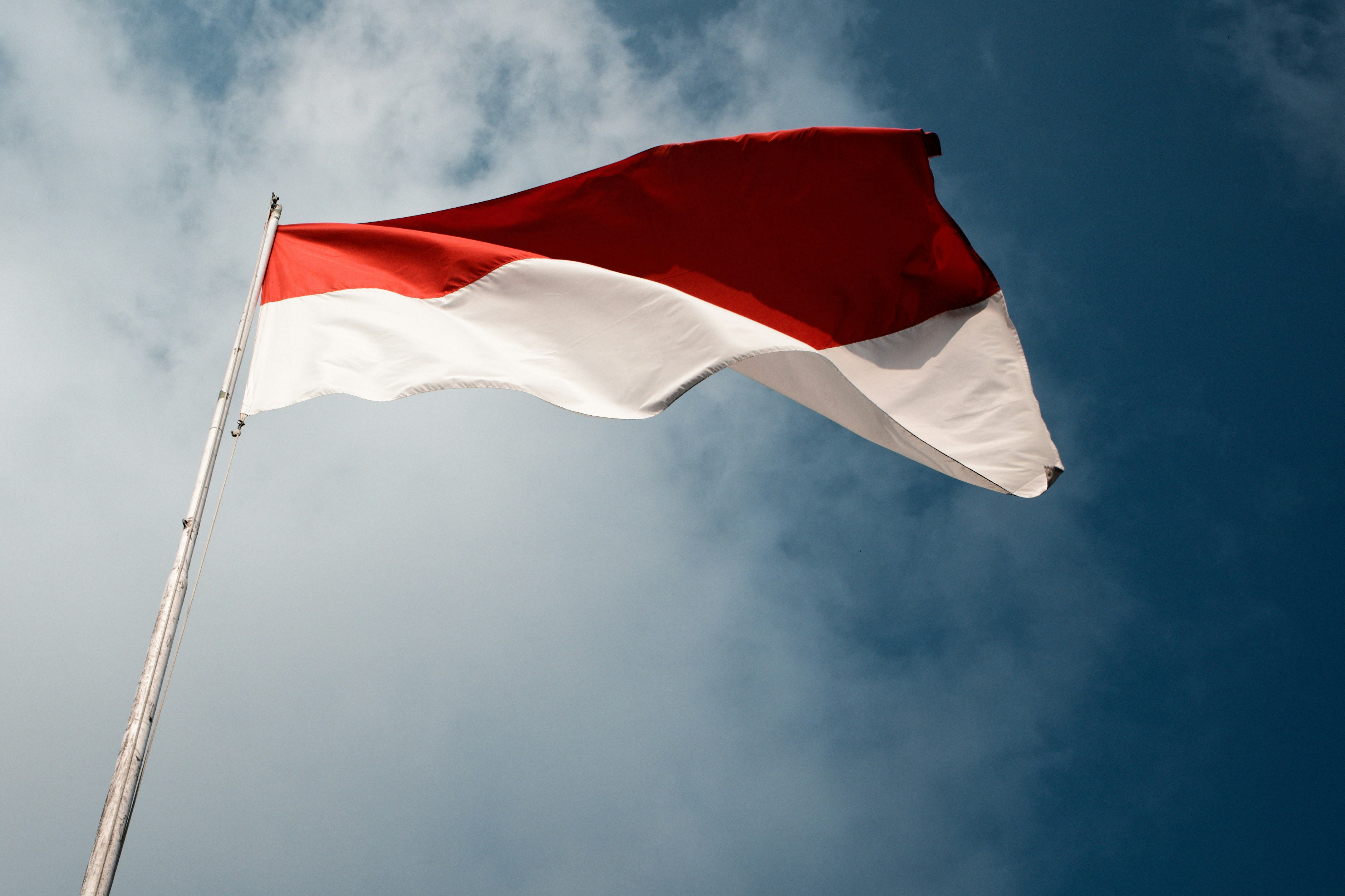 The red and white flag of Indonesia waving against a blue sky