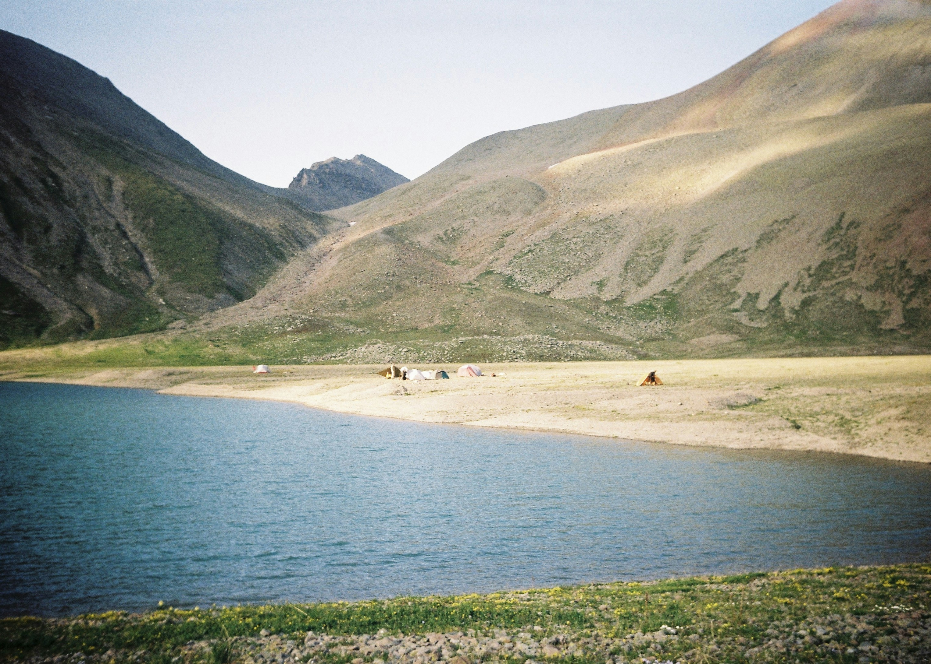 Small tents on a sandy lakeshore beneath high mountain slopes