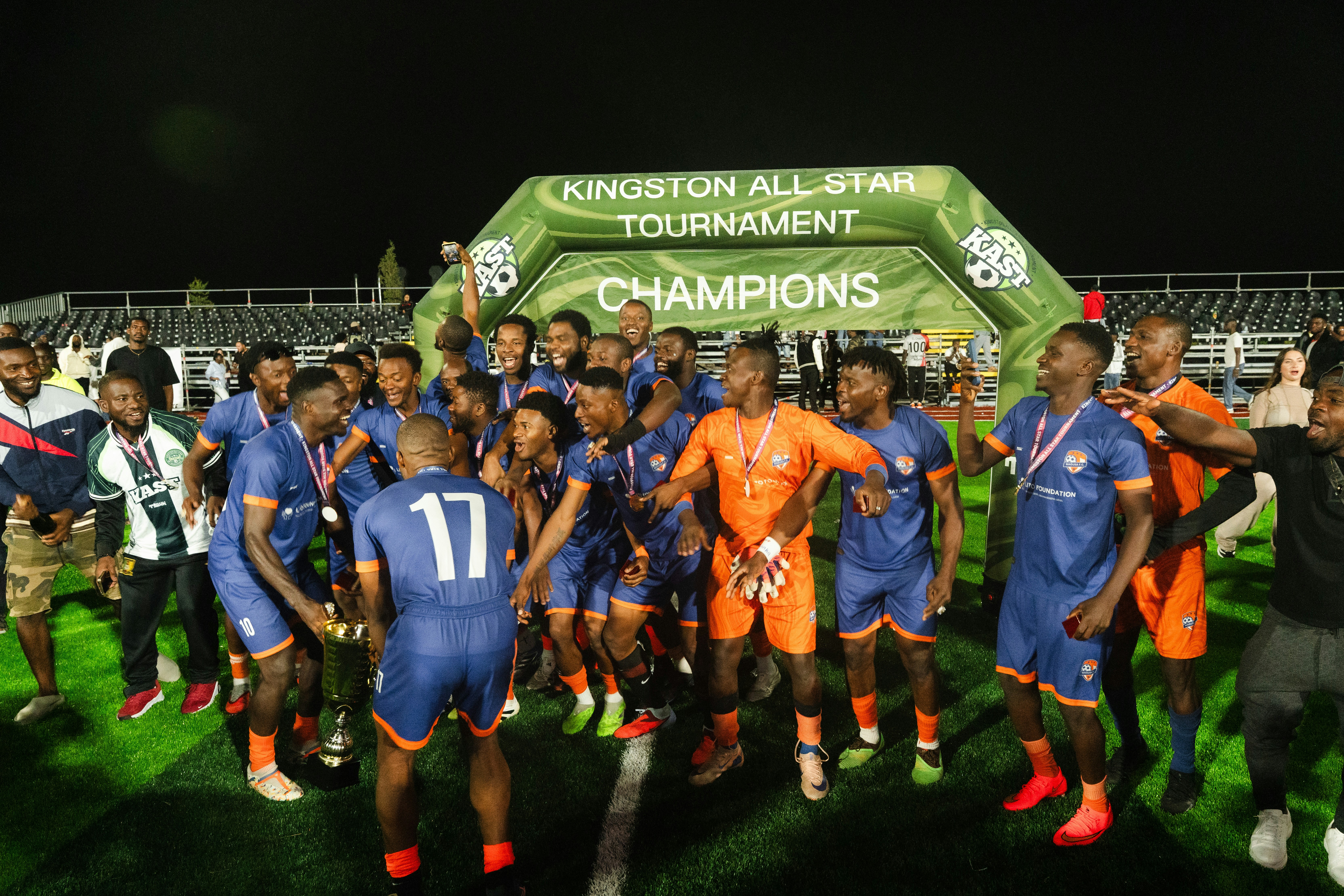 A soccer team celebrating with a trophy under a Kingston All Star Tournament arch
