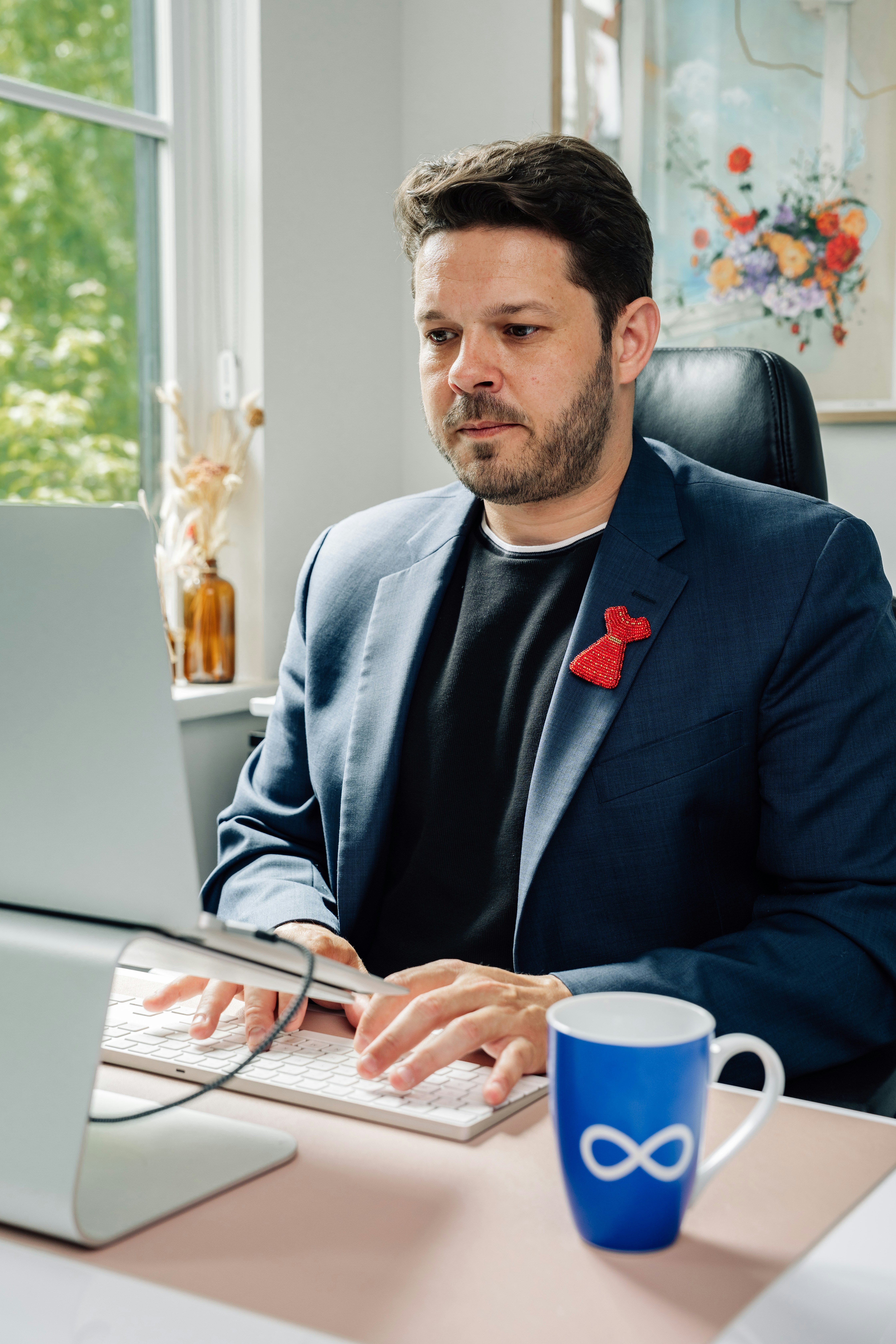 A man in a blue blazer typing on a laptop in a home office