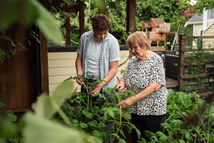 An adult and a teenager tending green plants in a backyard garden
