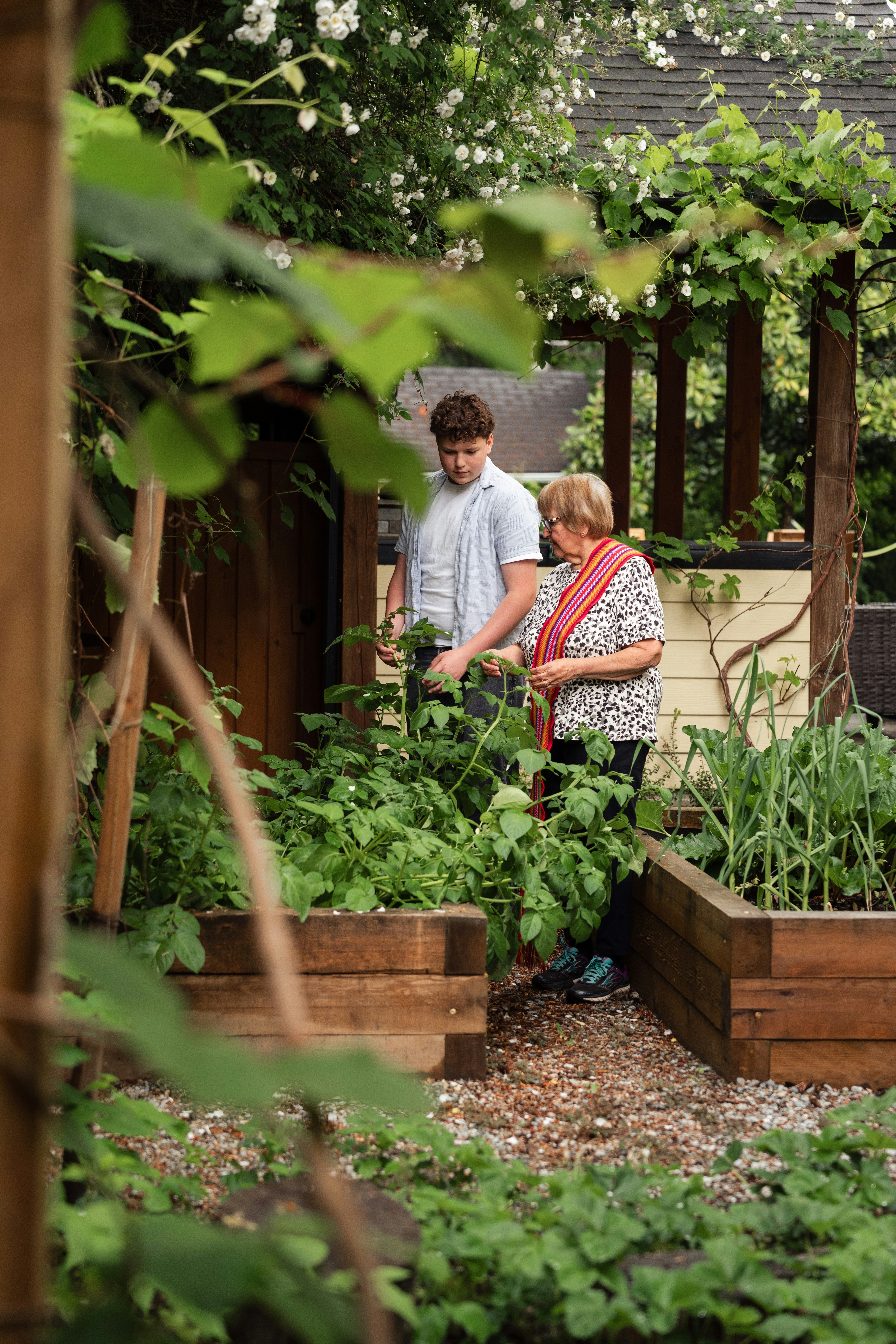 A teenager and an older woman tending to plants in a wooden garden bed