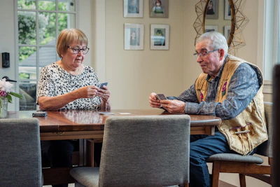 Two adults playing cards at a wooden dining table in a home