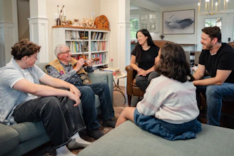 A family in a living room with an older man holding a violin