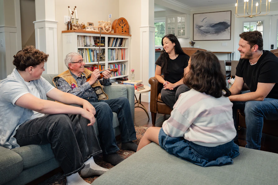 A family in a living room with an older man holding a violin