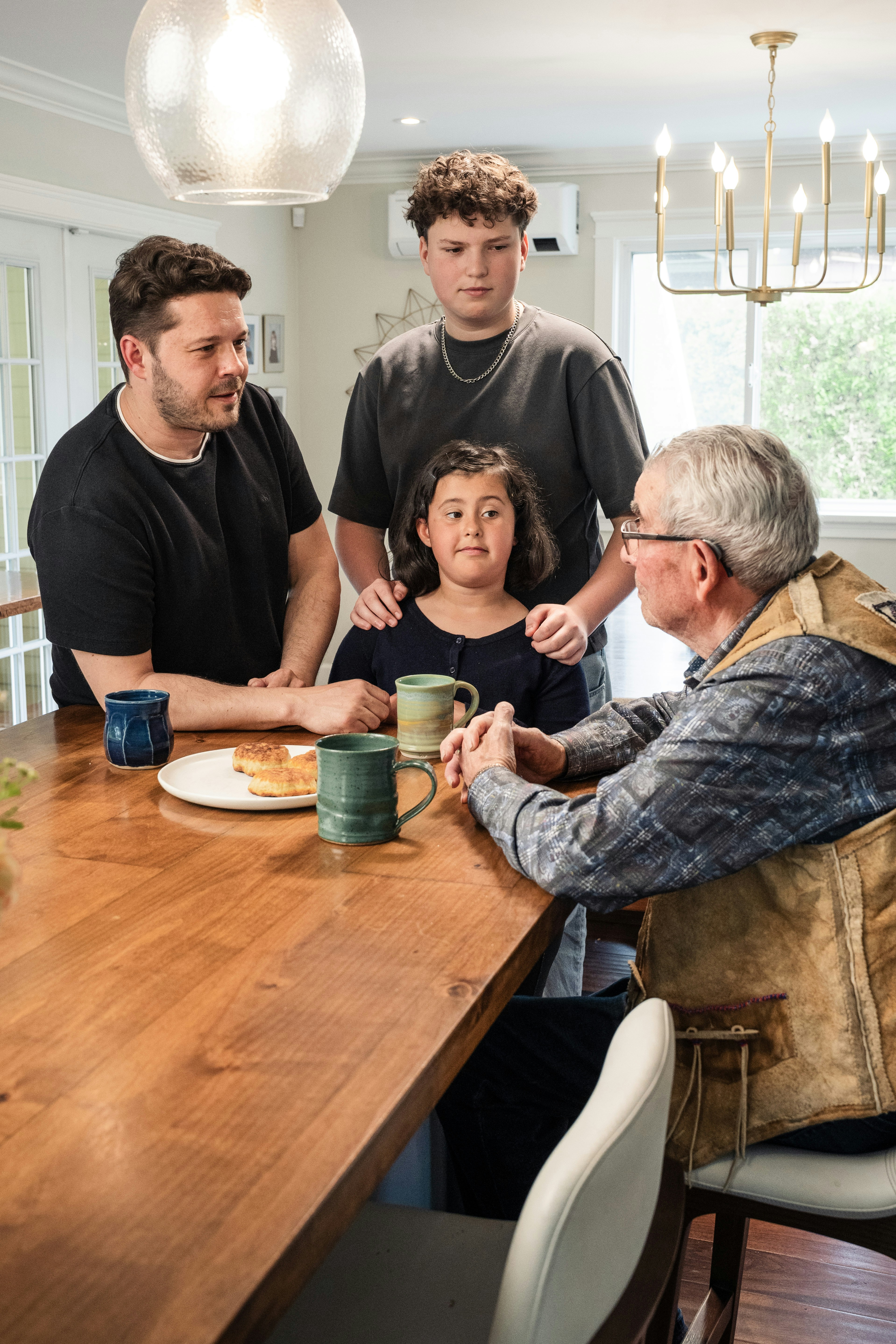 A family at a wooden table with mugs and a plate of food