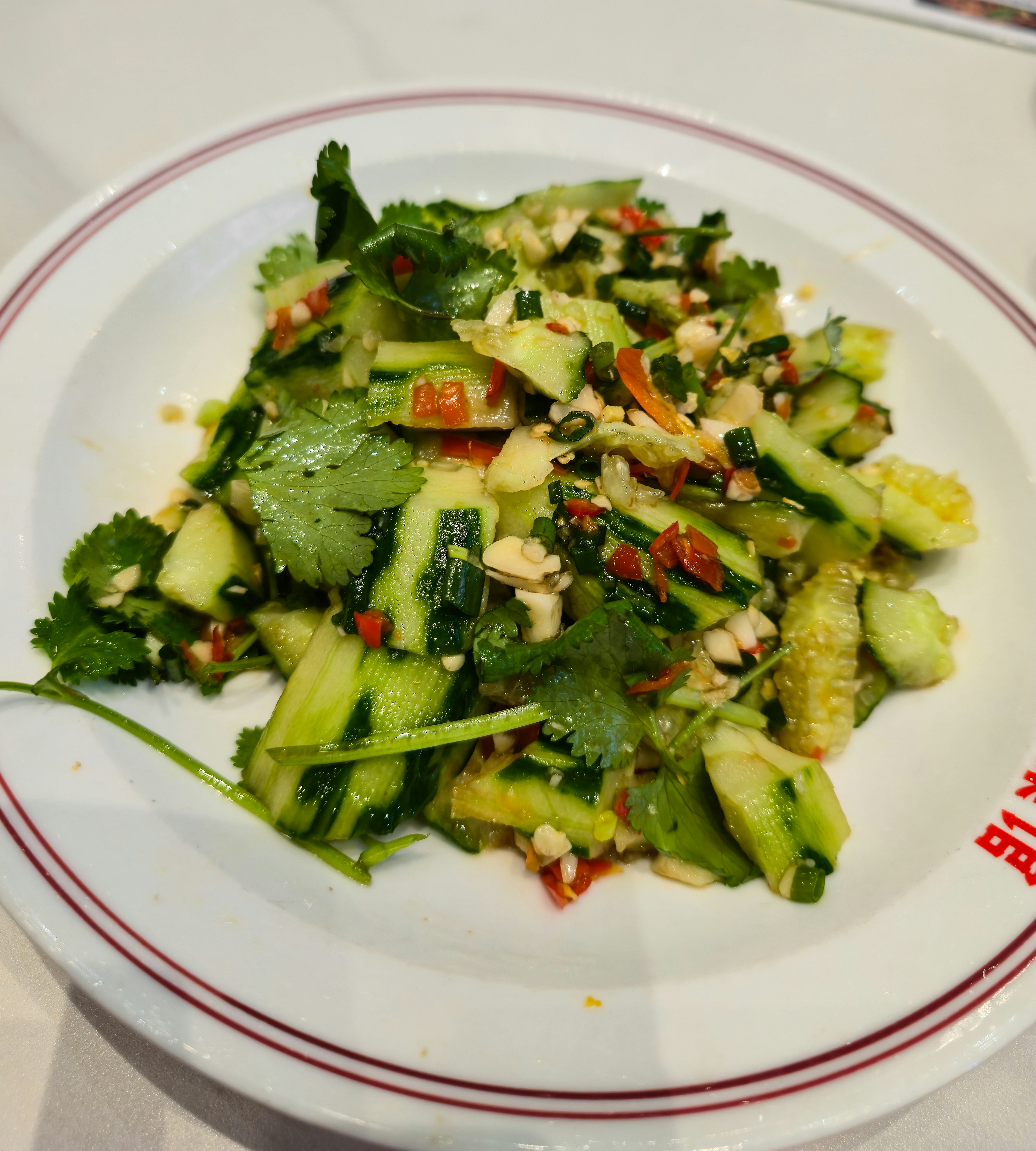 Zerdrückter Gurkensalat mit Koriander, Chili und Erdnüssen auf einem weißen Teller