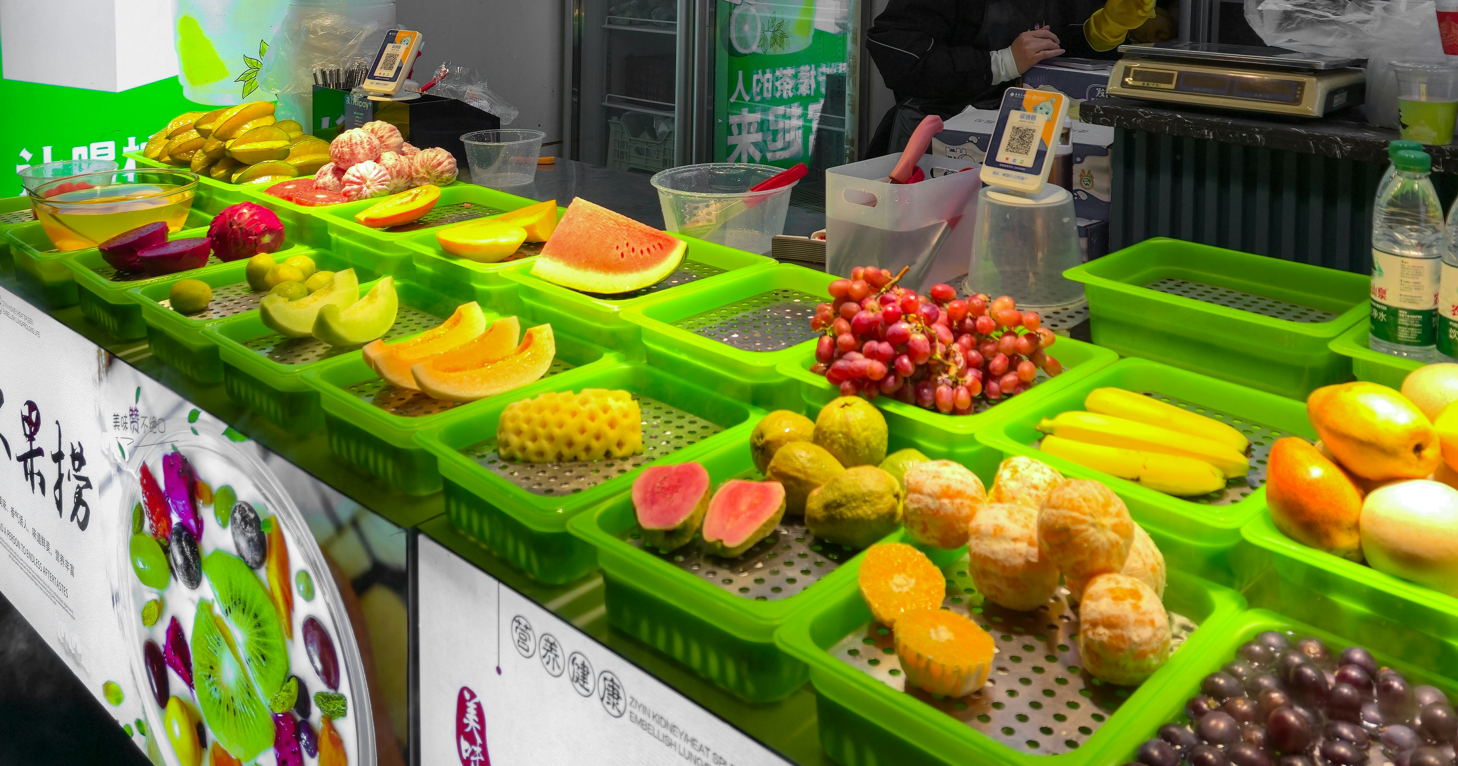 Frutas recém-cortadas em bandejas plásticas verdes em uma barraca de mercado em Chongqing