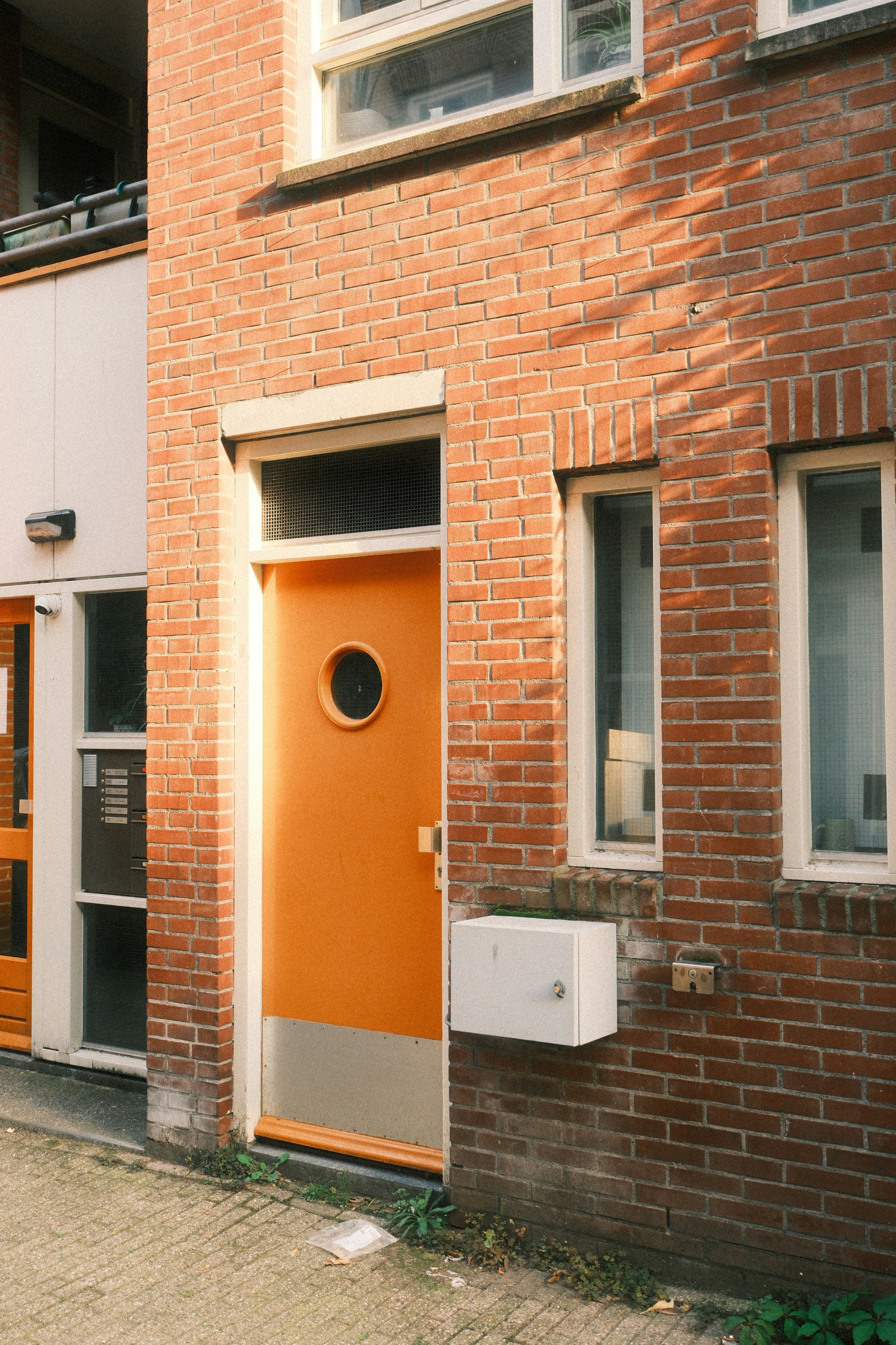 An orange door with a circular window in a red brick building facade