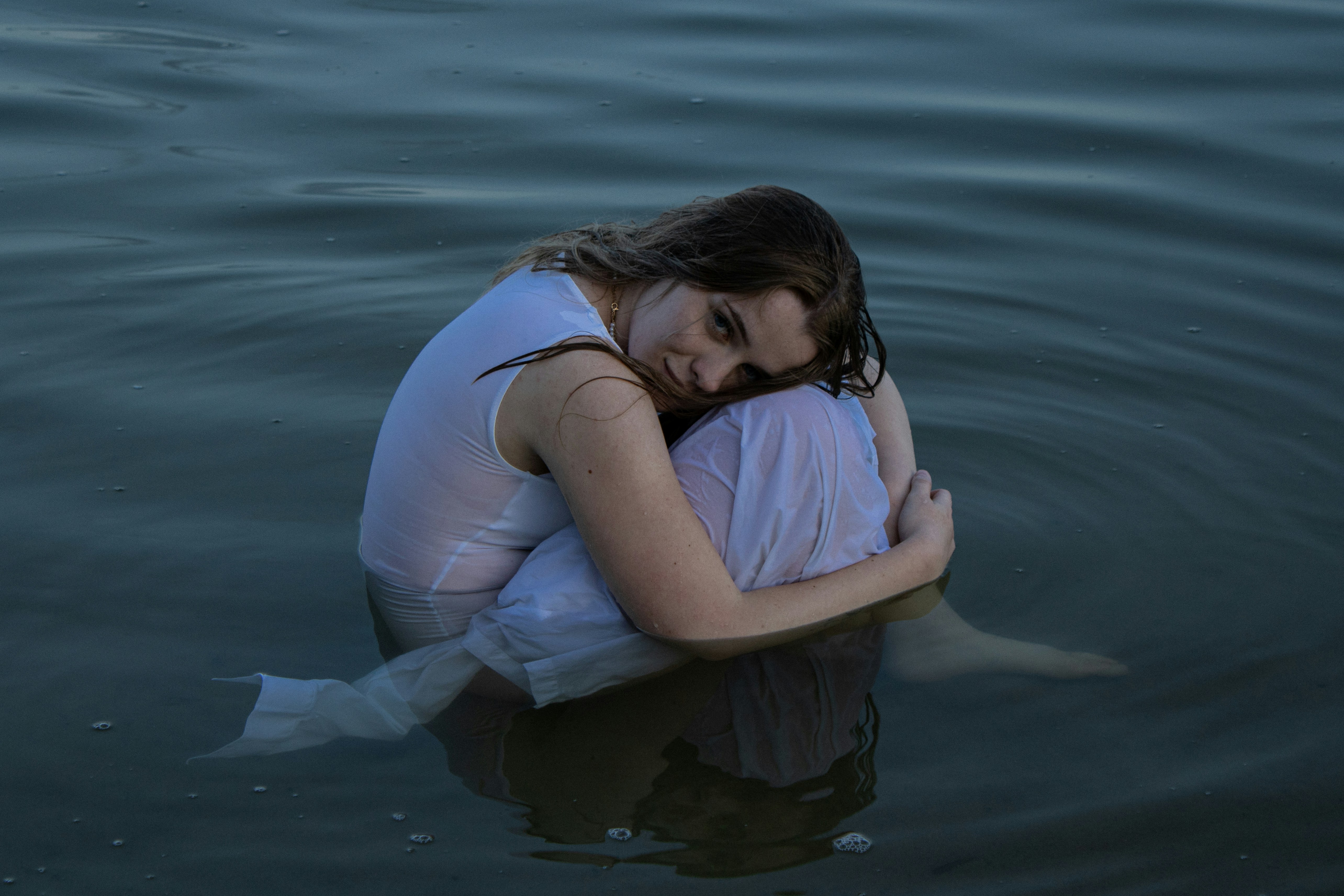 A woman in a white dress crouching in calm dark water