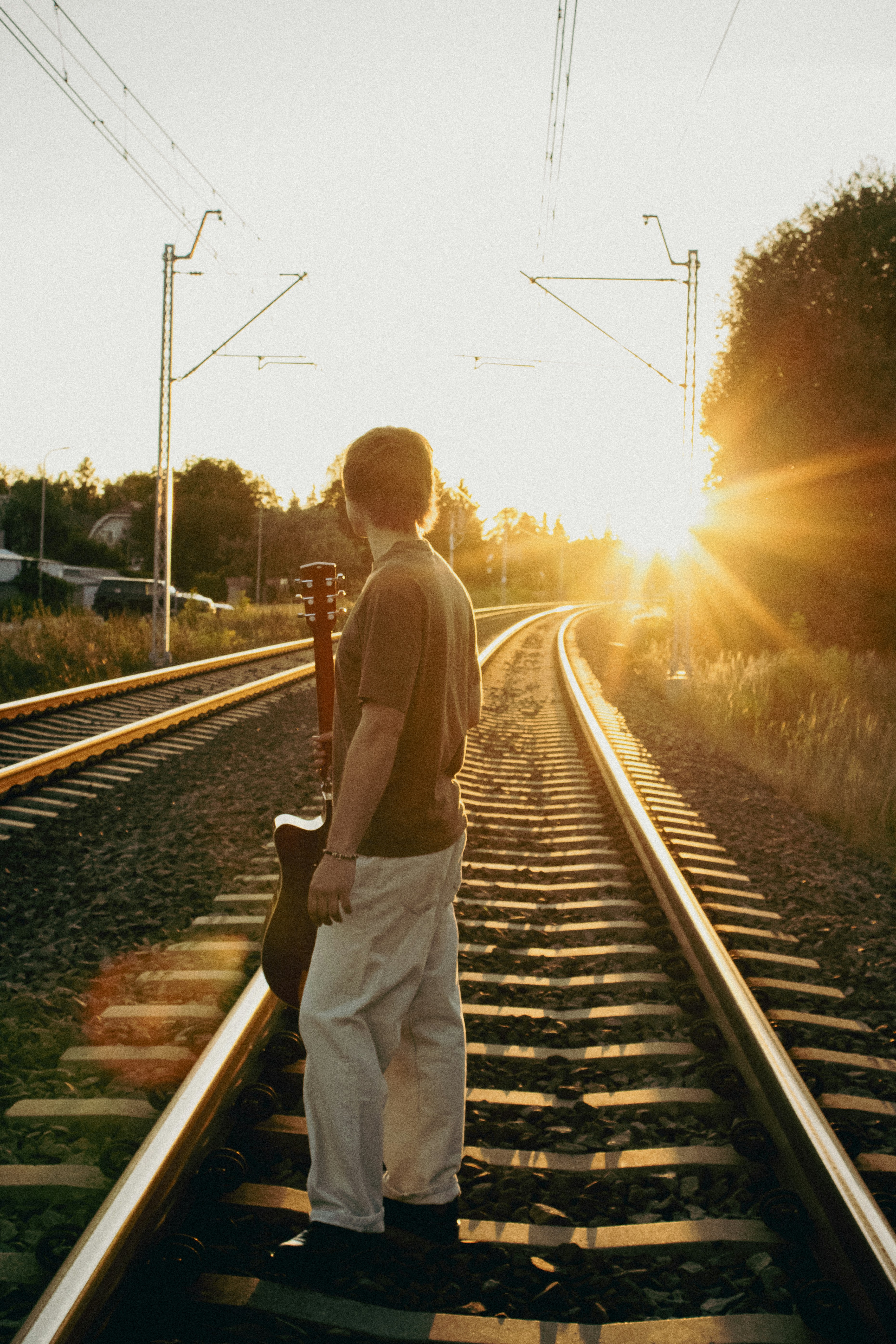 A person holding an acoustic guitar on railway tracks during golden hour